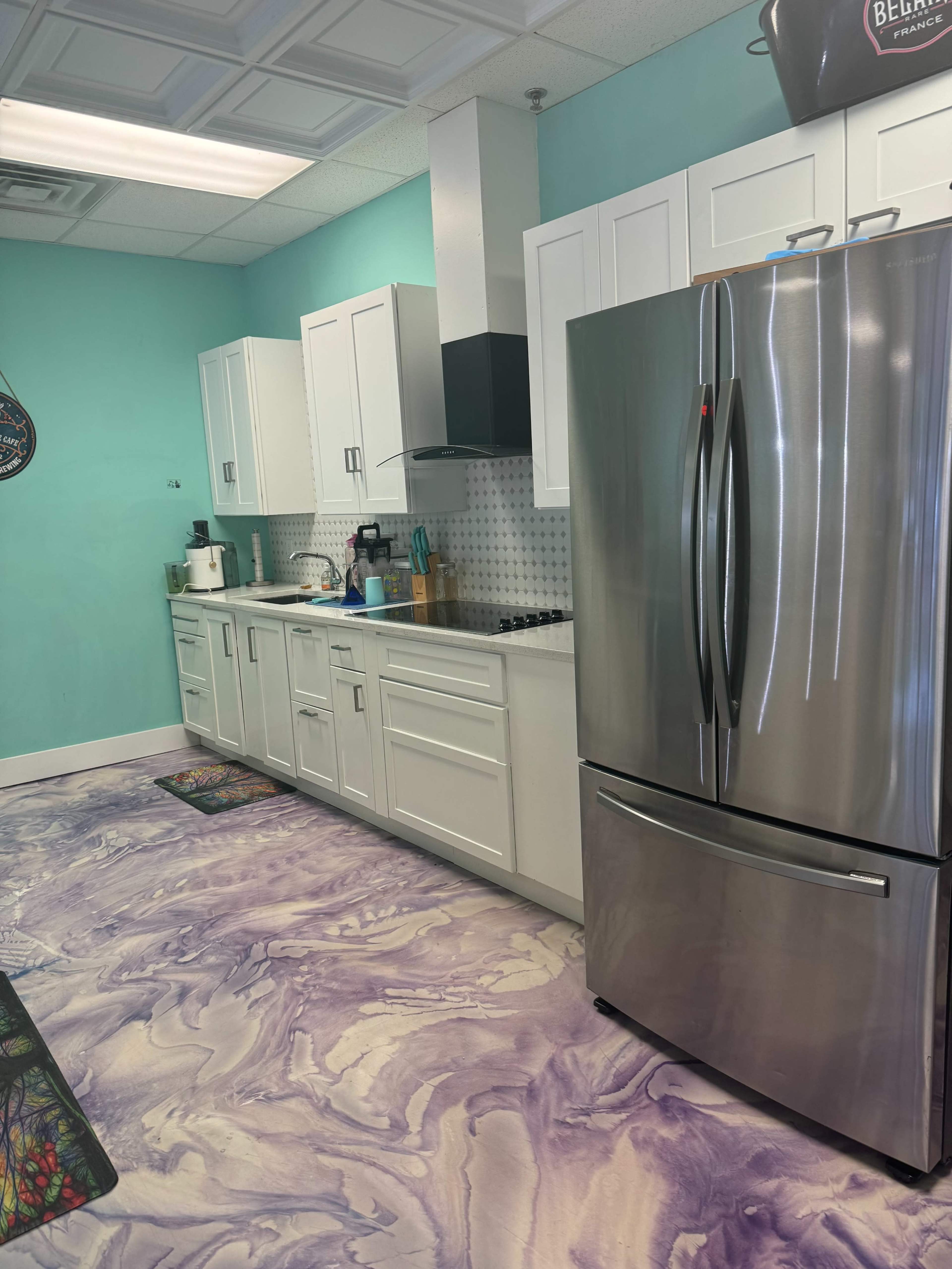A modern kitchen with light blue walls, white cabinets, a stainless steel refrigerator, and a marbled purple floor.
