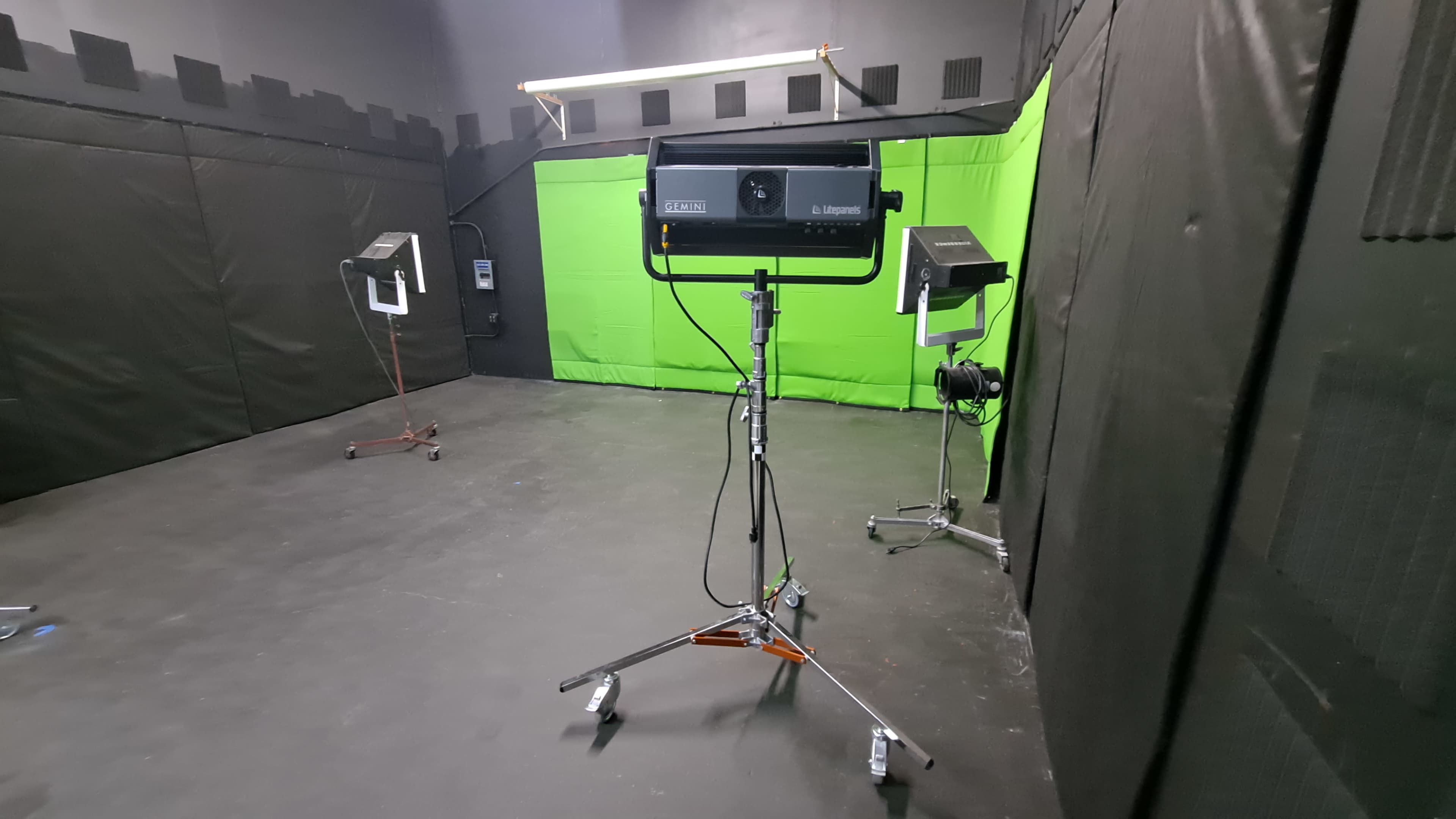 The image shows a room with a green screen backdrop and three lighting setups positioned on stands.