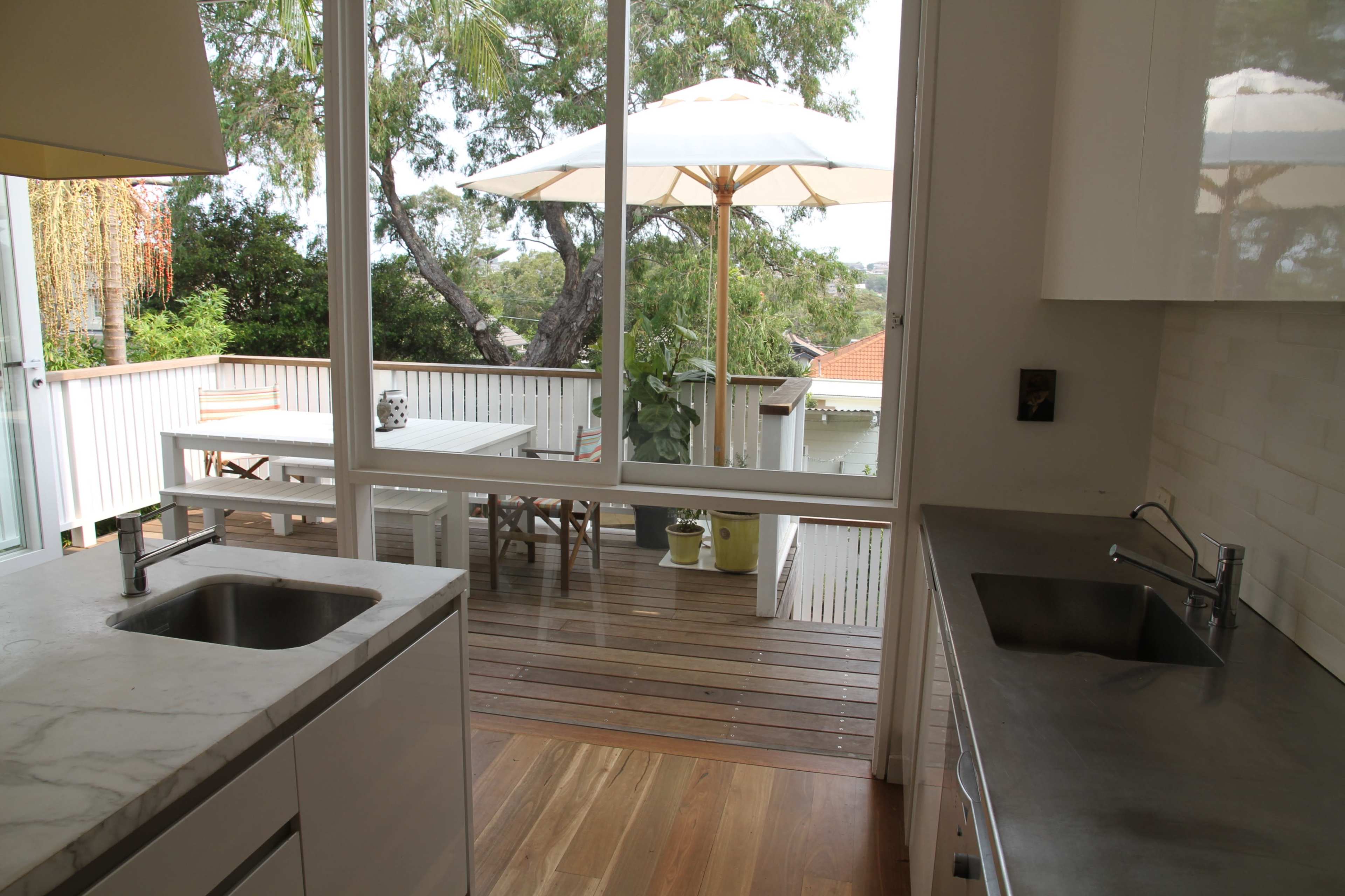 A modern kitchen with a view of a wooden deck and patio umbrella through large glass doors.