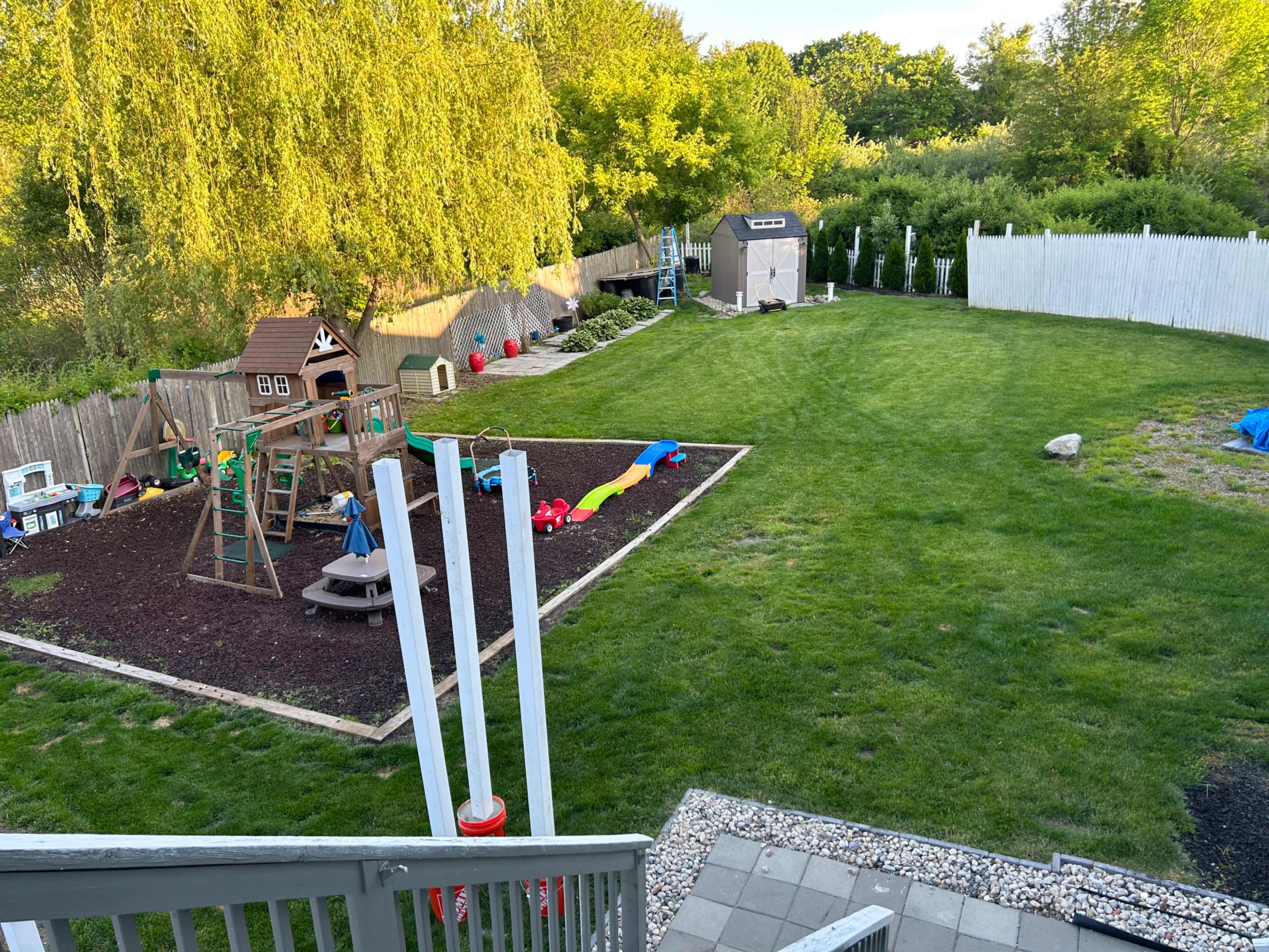 A backyard play area featuring a playground structure, a sandbox, and colorful play equipment set on grass.