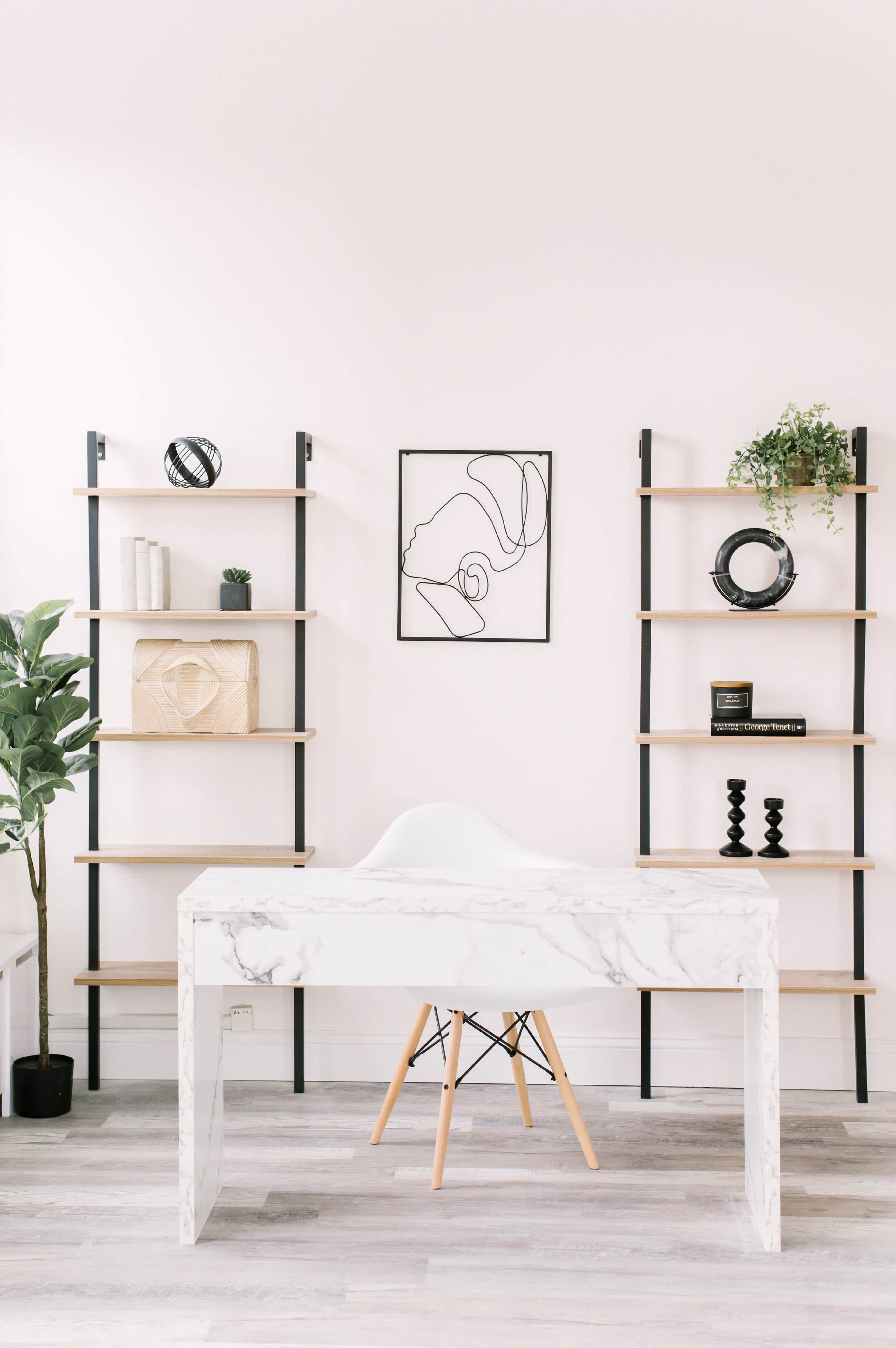 A minimalist office space features a marble-topped desk with an Eames-style chair, flanked by two tall wooden shelving units, and adorned with a line art drawing on the wall.