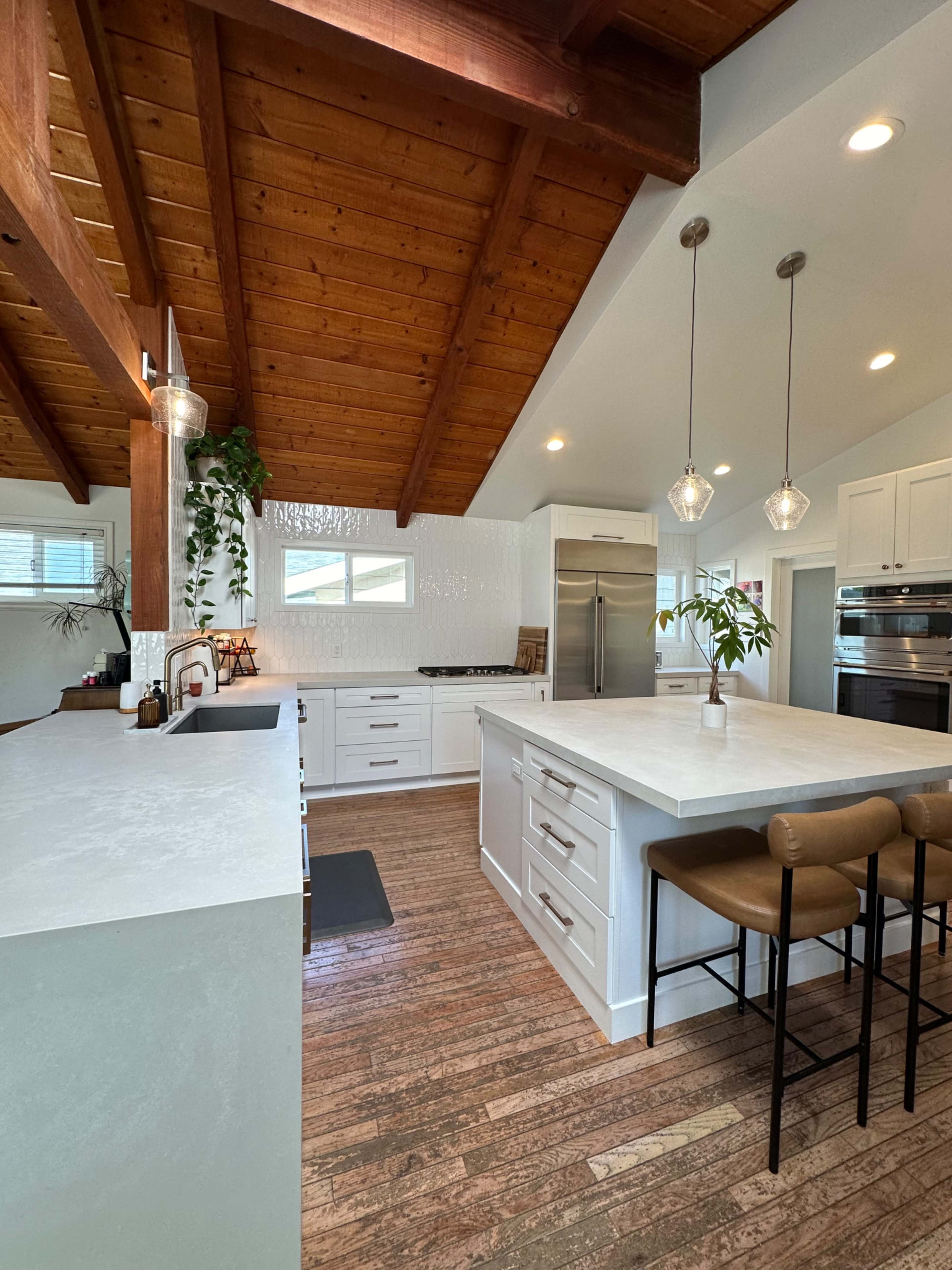 A modern kitchen featuring a large island with bar stools, wooden beams on the ceiling, and sleek cabinetry.