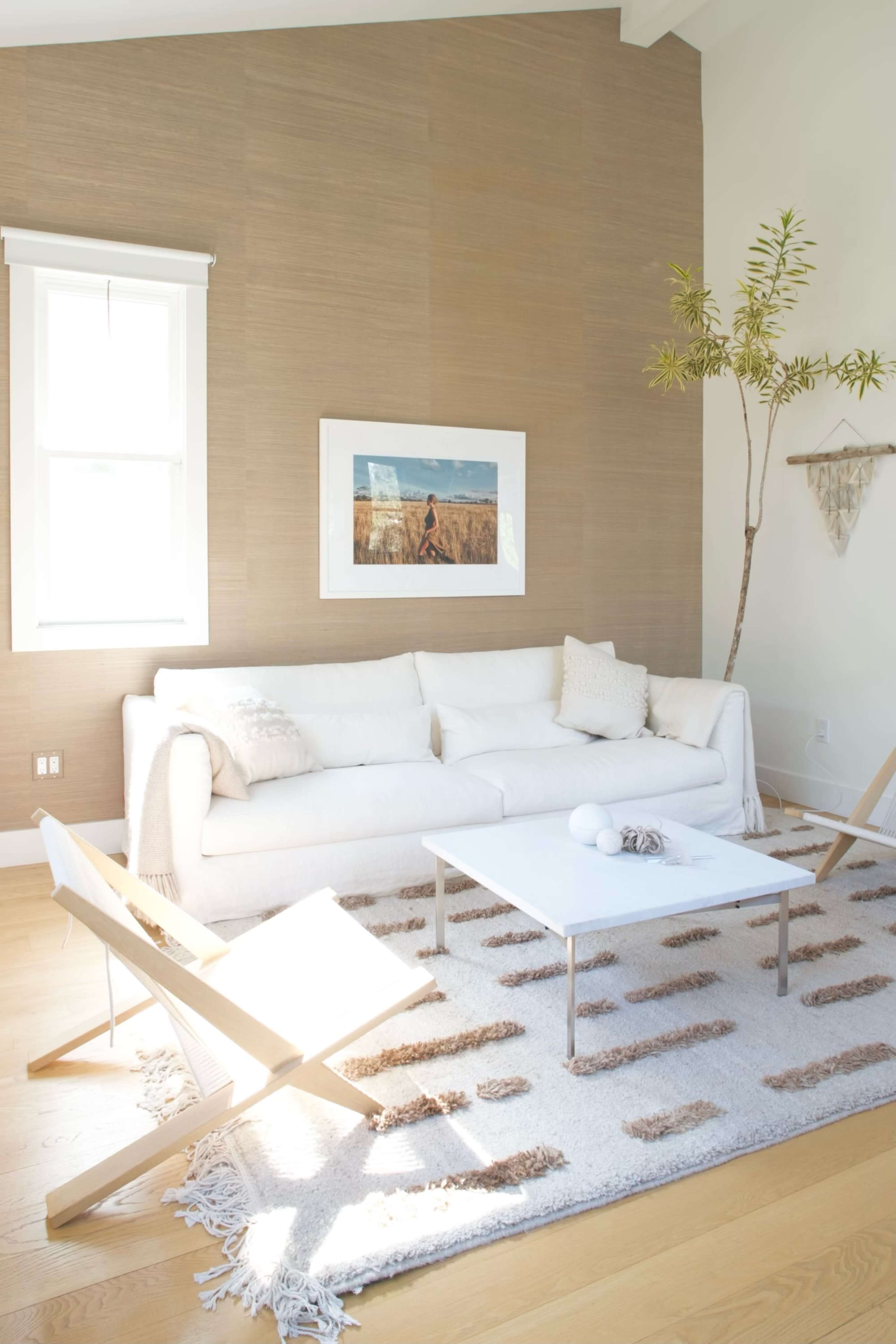 The living room features a white sofa, a glass coffee table, and a rug with a pattern, illuminated by natural light through a window.