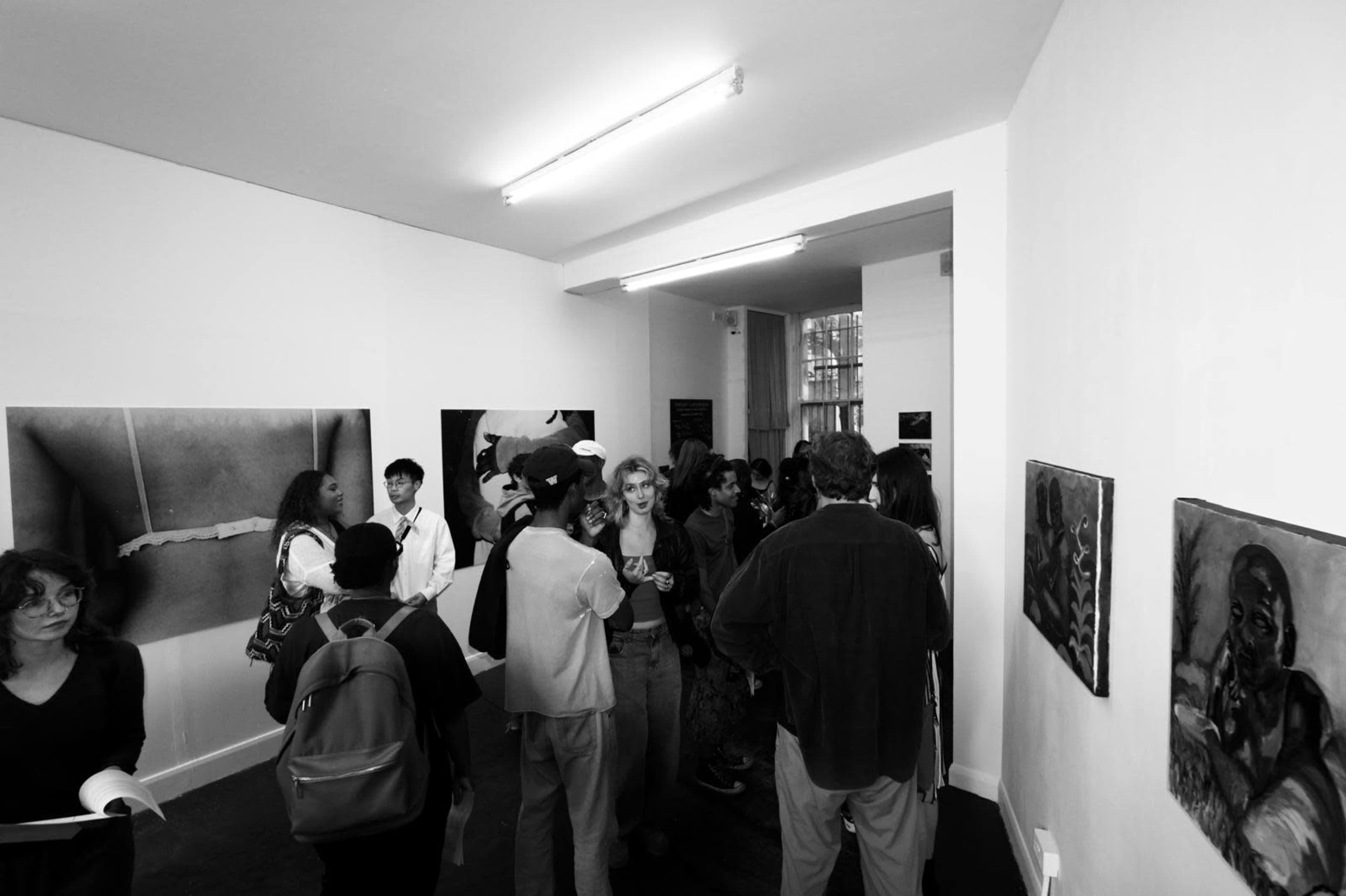 A crowd of people gathers in an art gallery featuring several framed artworks on the walls.