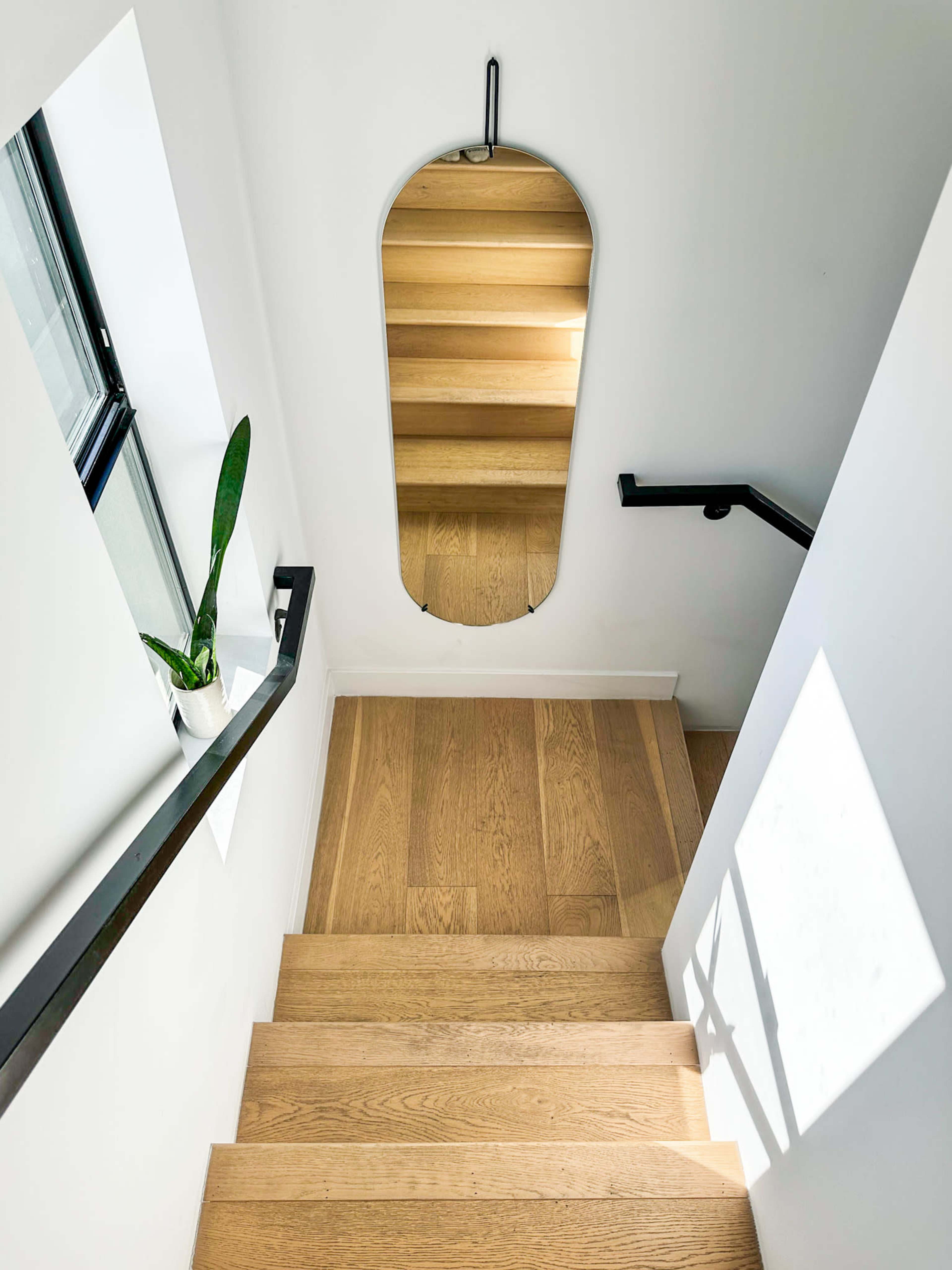 A staircase with wooden steps leads down to a landing, featuring a large mirror mounted on the wall and a potted plant on the railing.