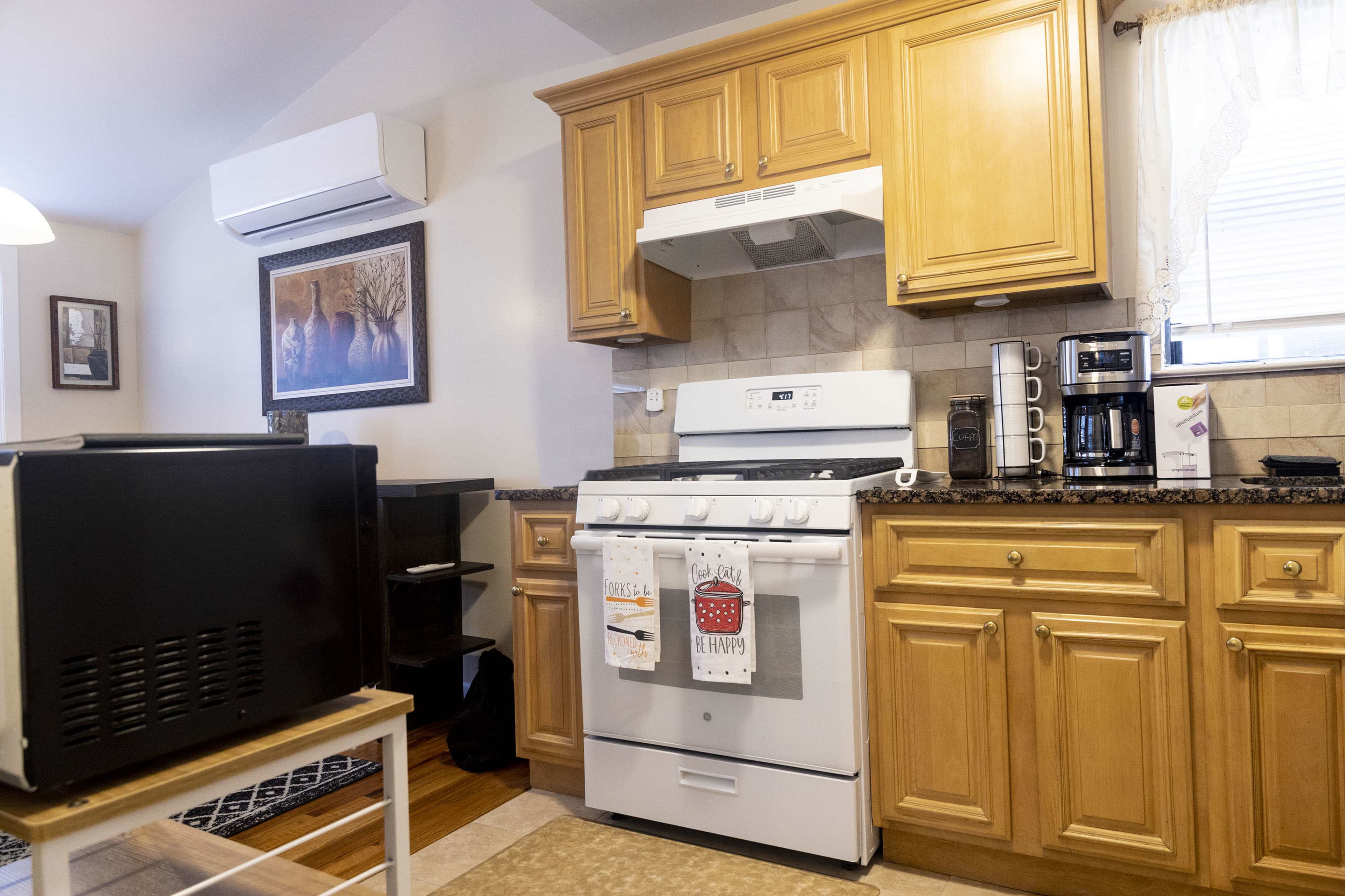 A kitchen with wooden cabinets, a gas stove, a microwave above it, and various appliances on the countertop, including a coffee maker.