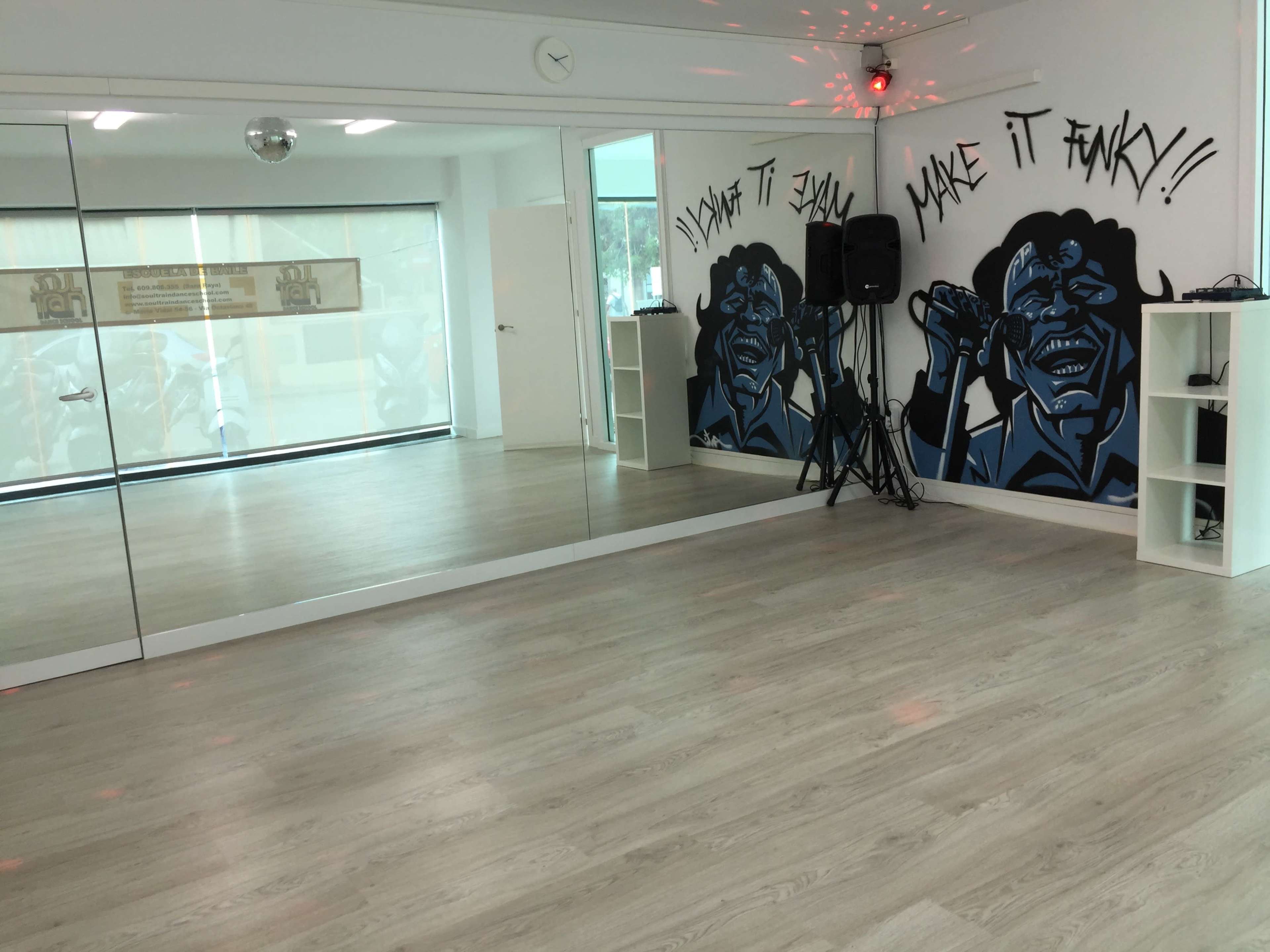 A dance studio with a large mirror, a sound system, and a wall mural featuring a blue-faced character.