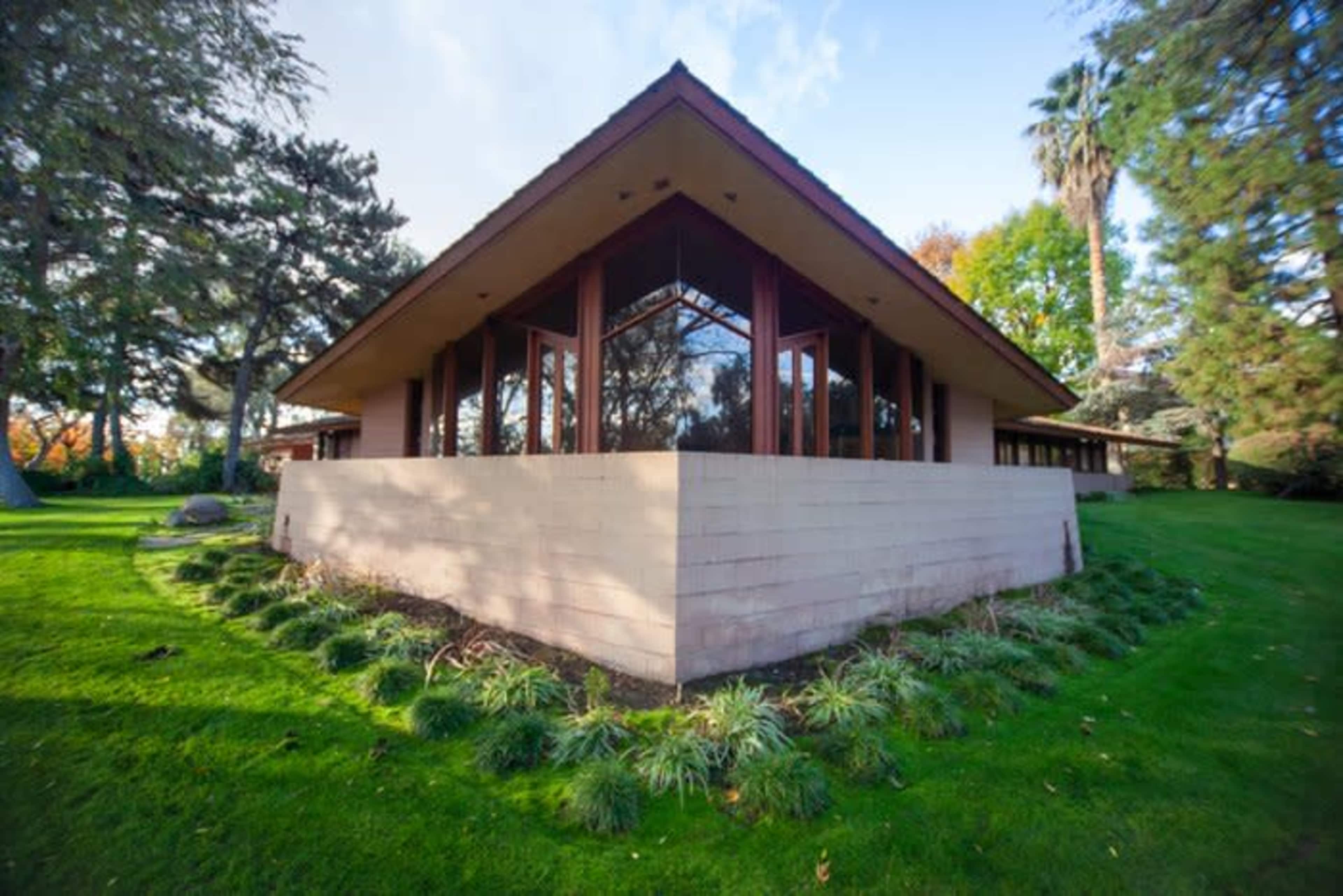 A modern, angular house with large windows sits on a lush green lawn surrounded by trees.