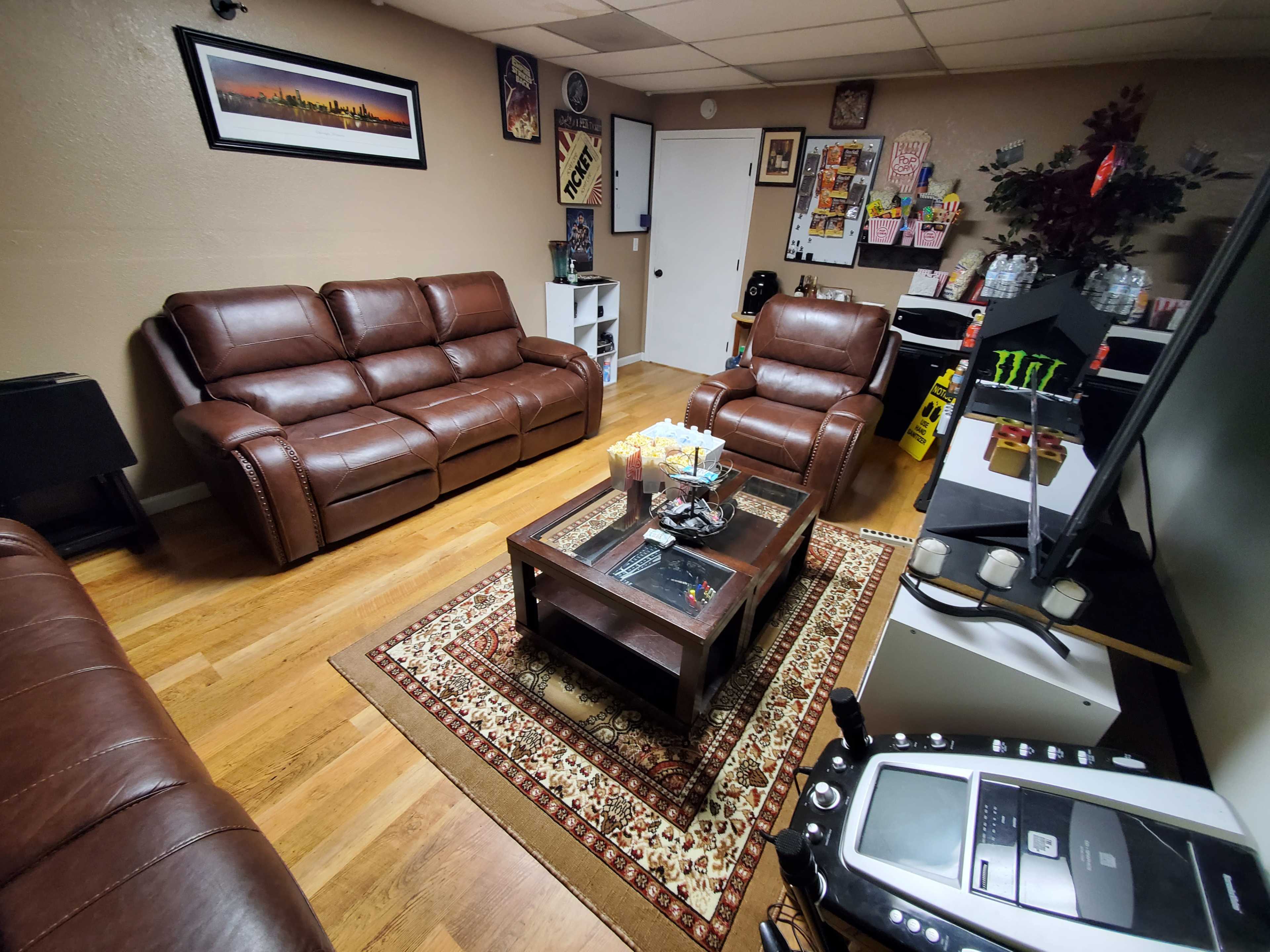 A living room with brown leather sofas arranged around a coffee table on a patterned rug, with various decorations and a TV in view.
