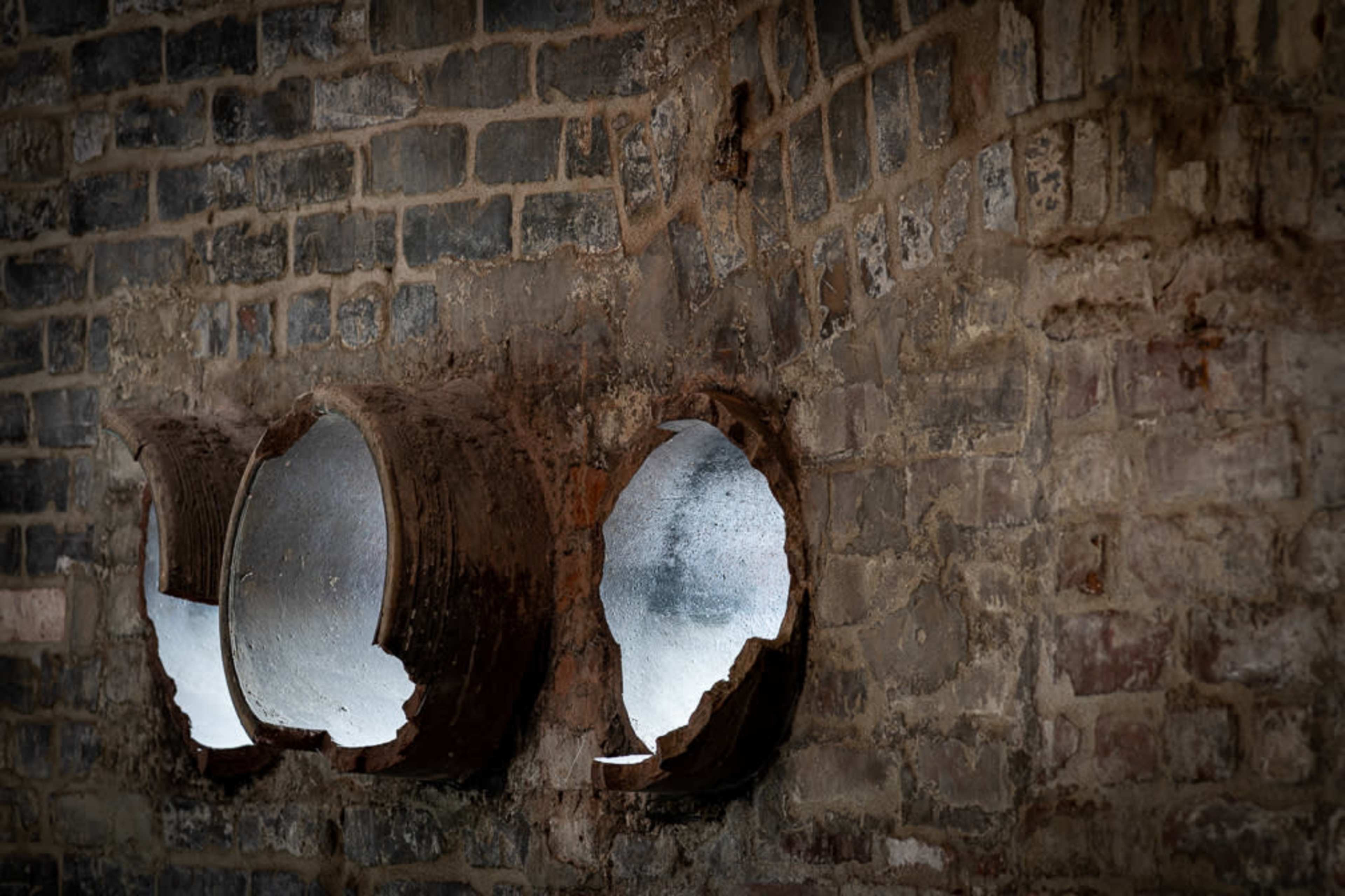 Three circular openings in a weathered brick wall, partially surrounded by peeling plaster.