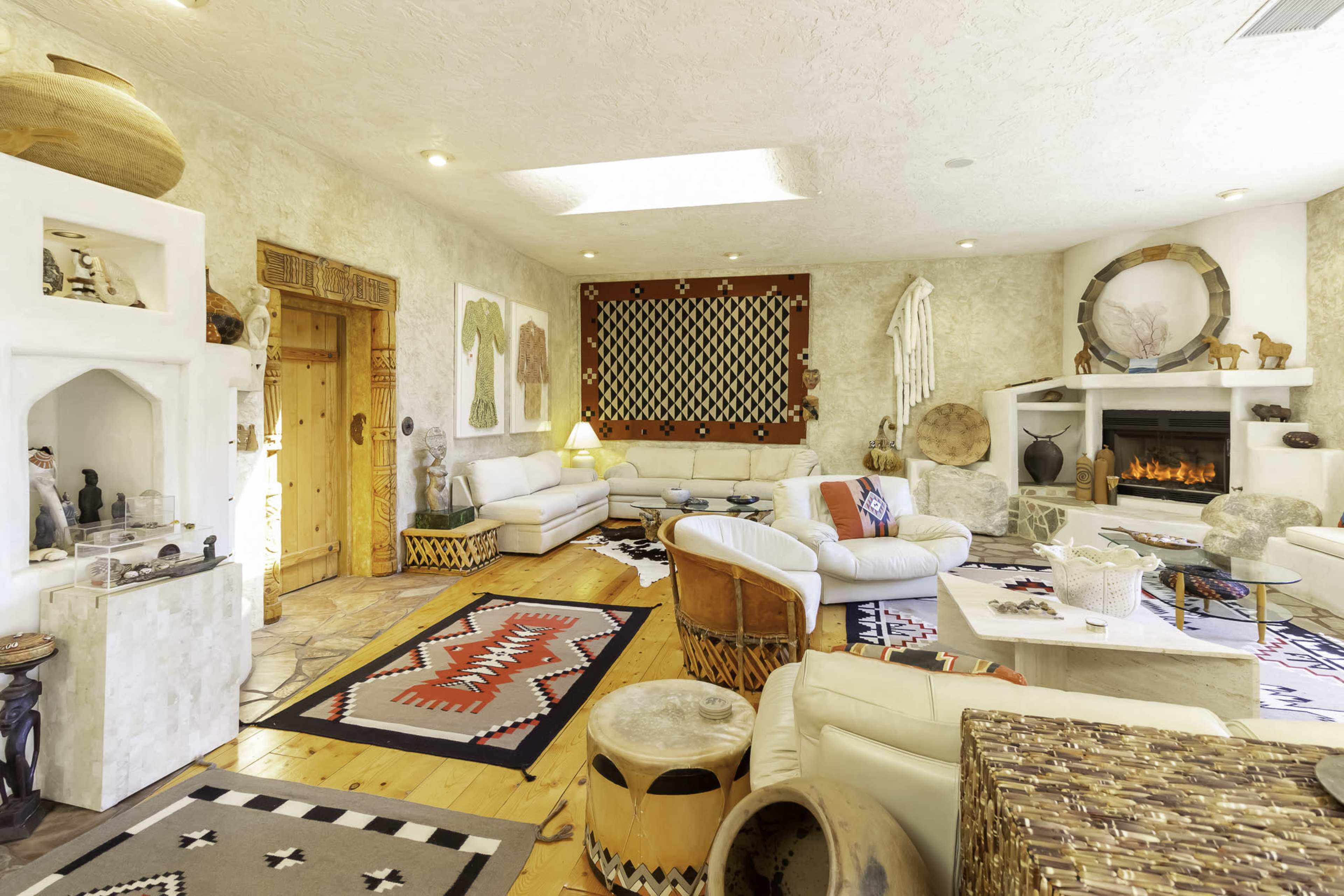 A spacious living room features white furniture, tribal patterns on the rugs, and decorative artifacts on the walls and shelves.