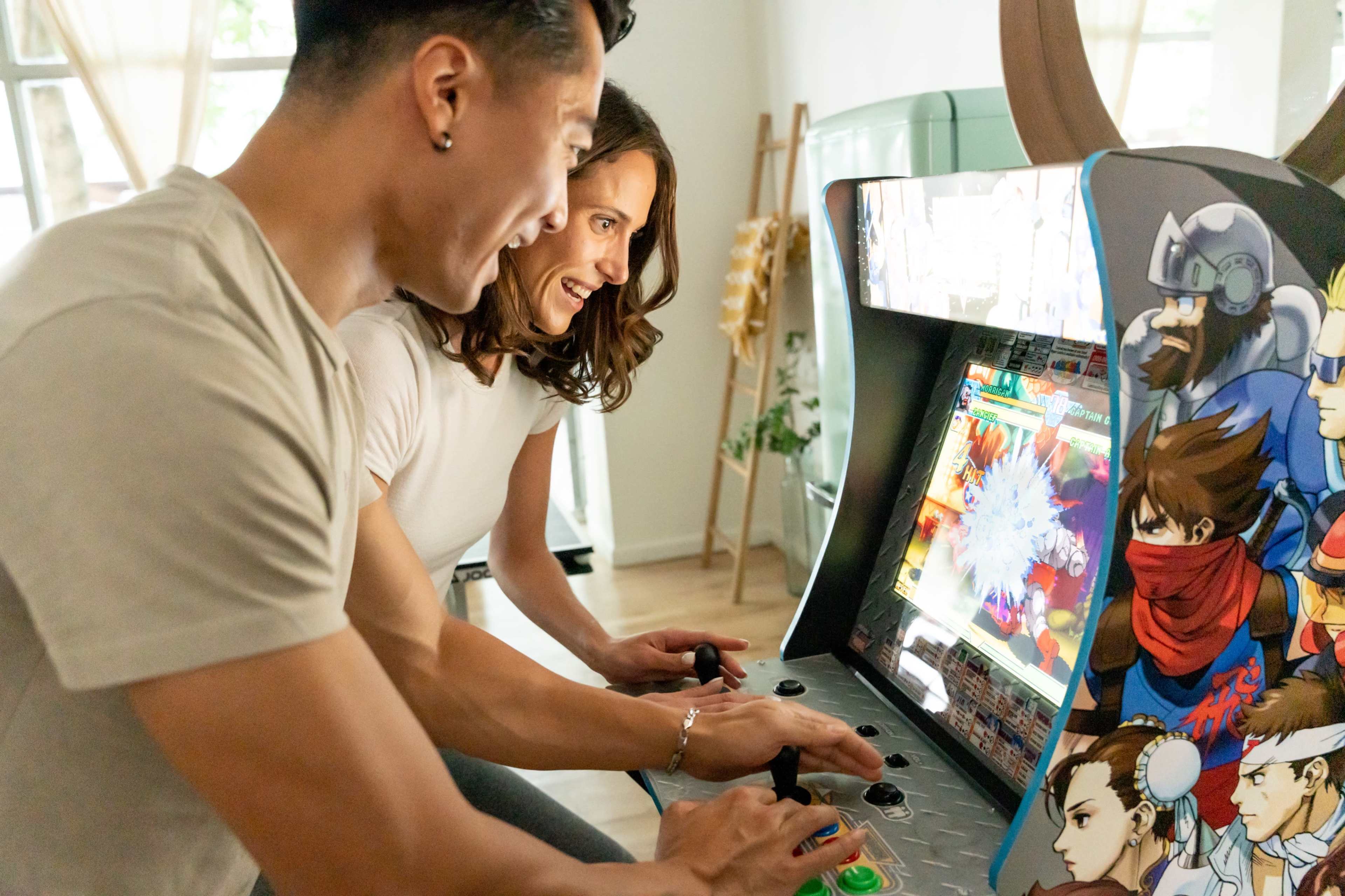 A man and woman are playing a classic arcade game, focused on the screen and using the game controls.