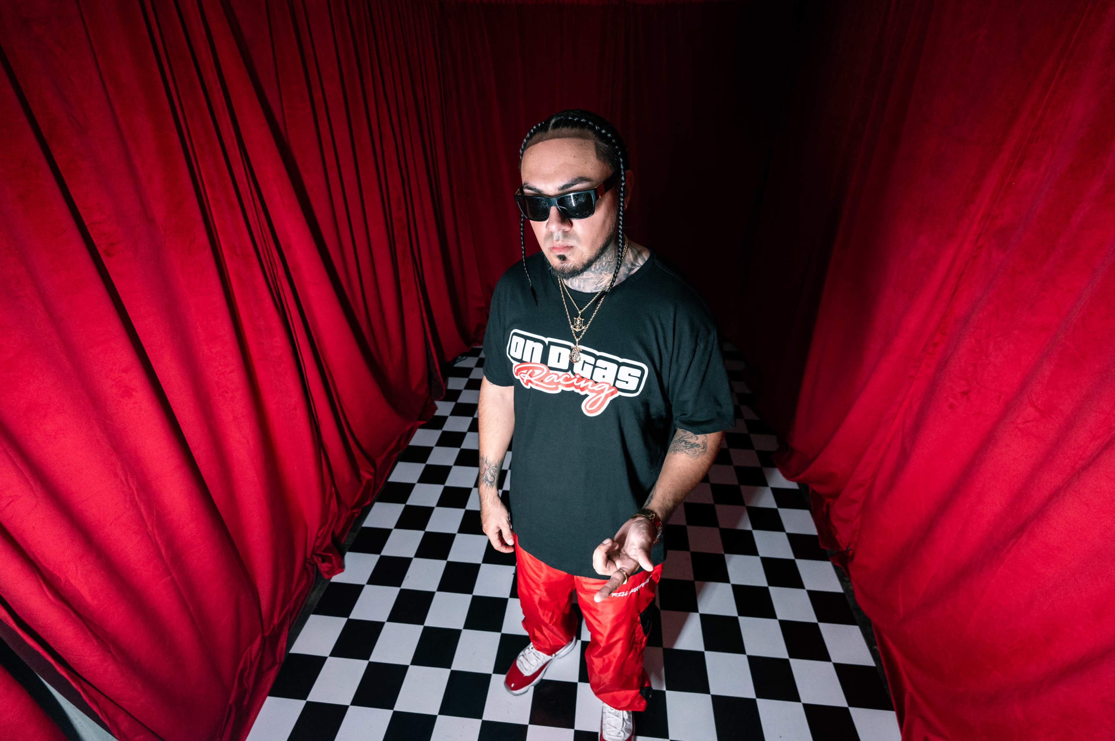 A person wearing a black t-shirt and red pants stands in a room with red curtains and a checkered floor.