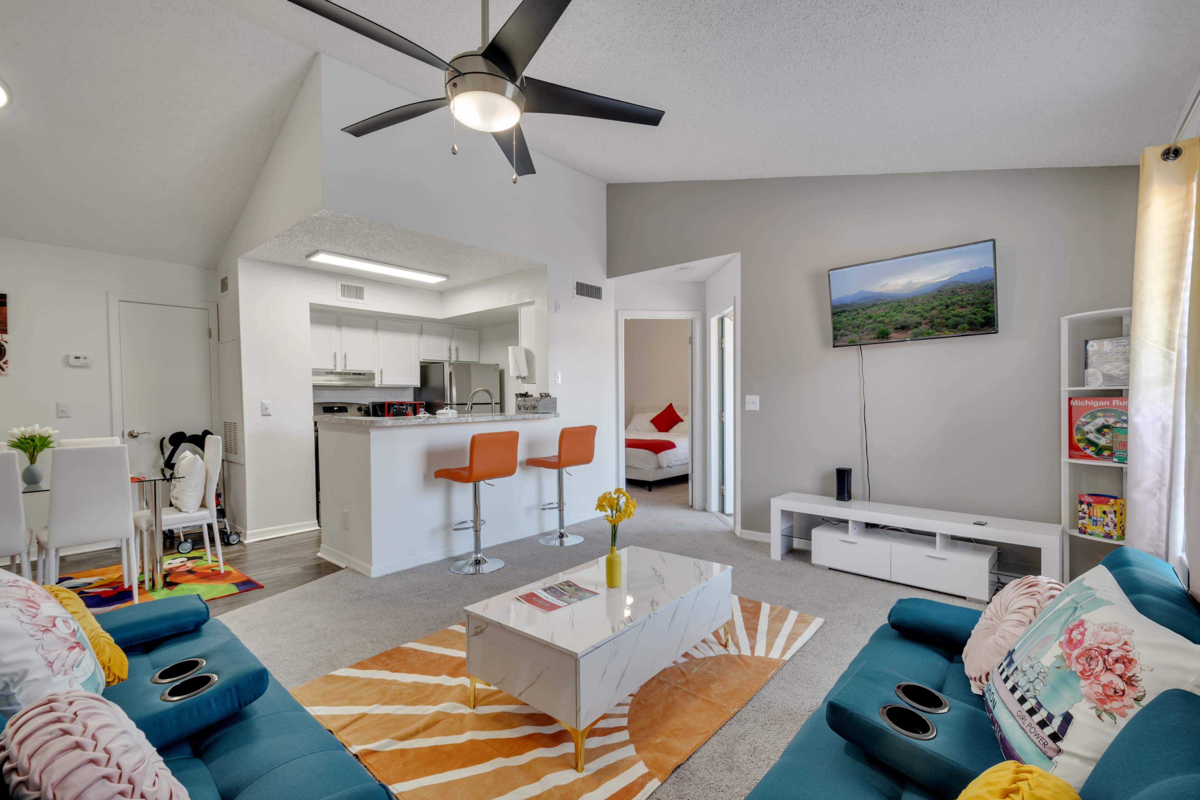 A modern living room with two blue sofas, a white coffee table, and an open kitchen area, complete with a dining table and bar seating.