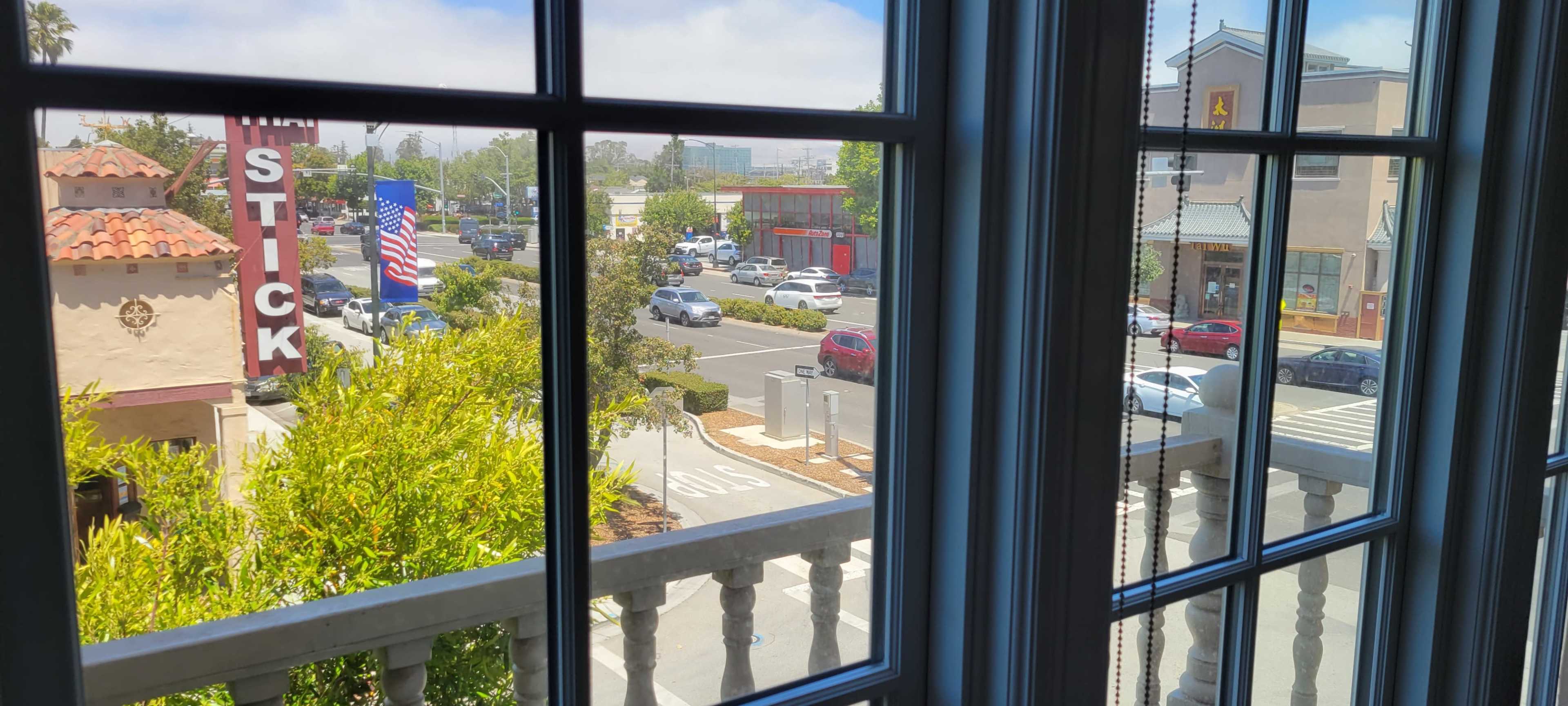 The view from the window shows a bustling street with parked cars and a building featuring an American flag.
