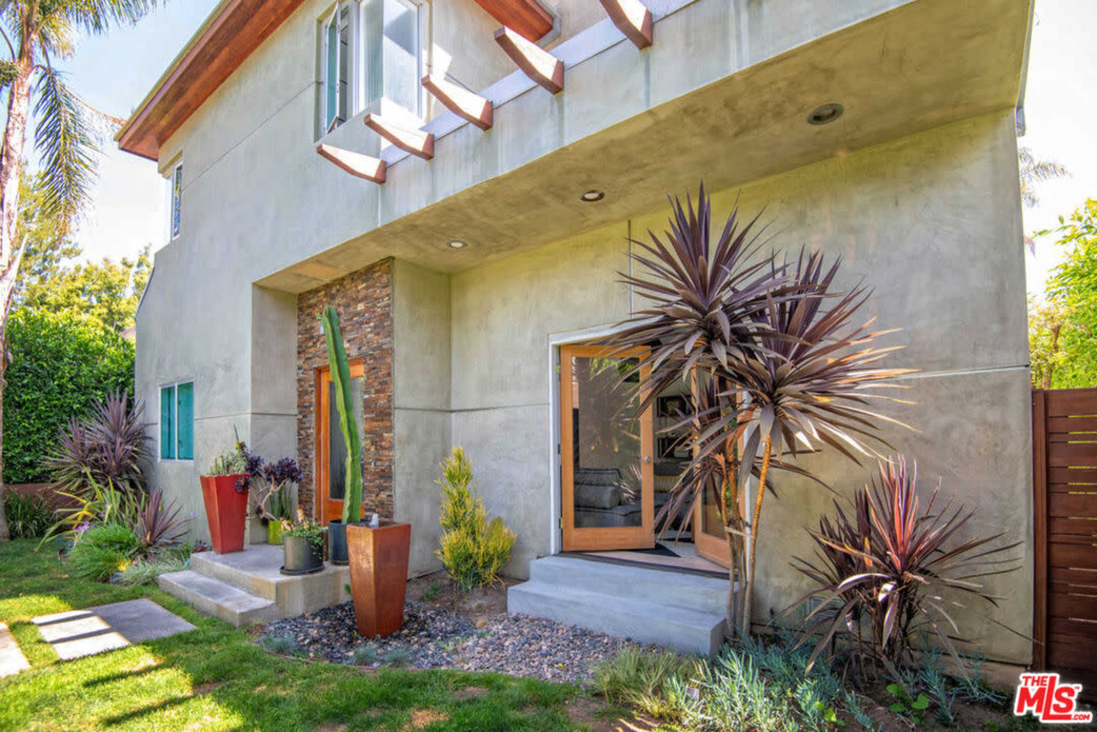 The entrance of a modern house featuring a concrete exterior, wooden accents, and landscaped greenery.