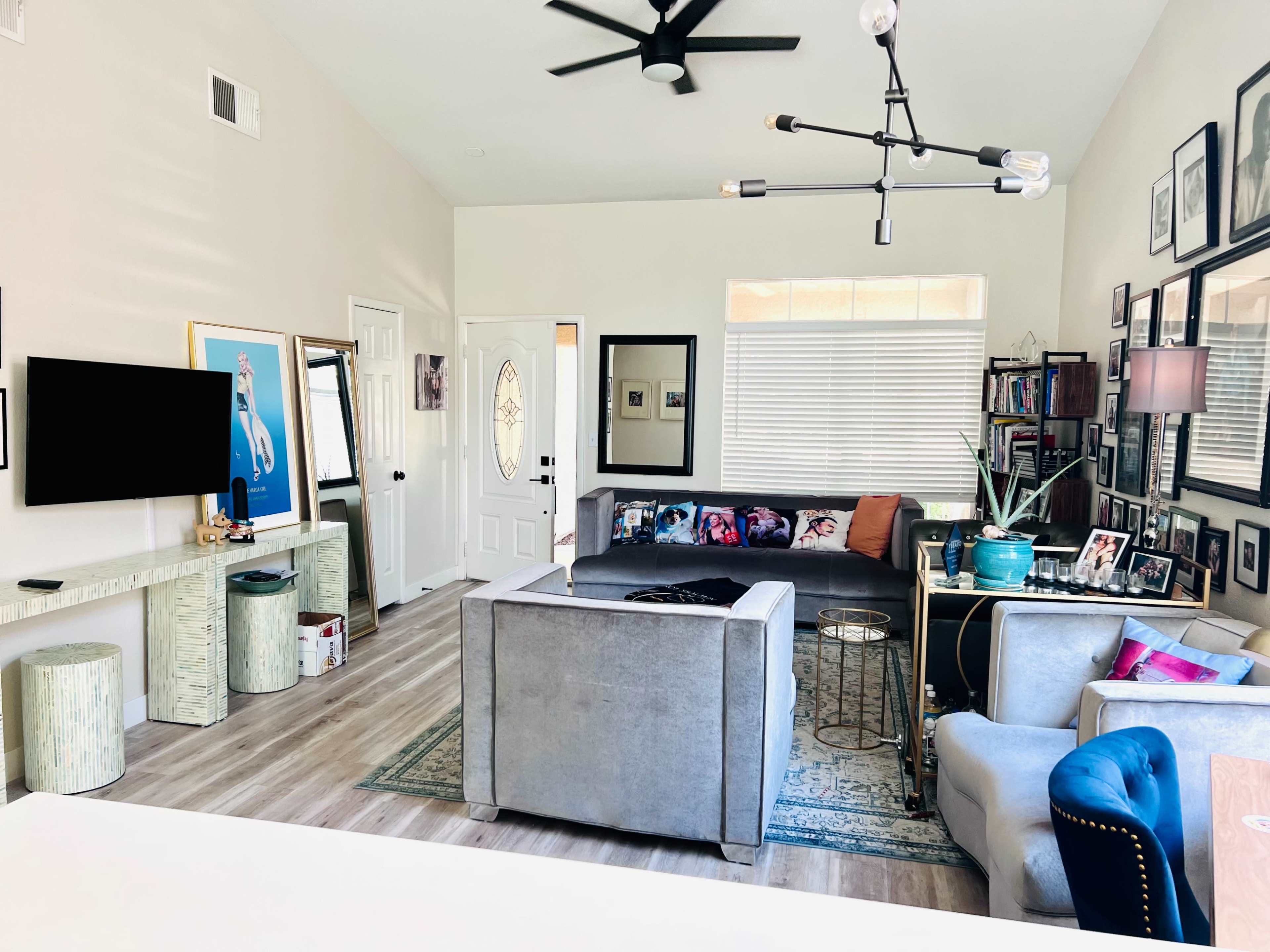 The room features a spacious layout with a mix of seating areas, a television on the wall, and various framed photos on display.