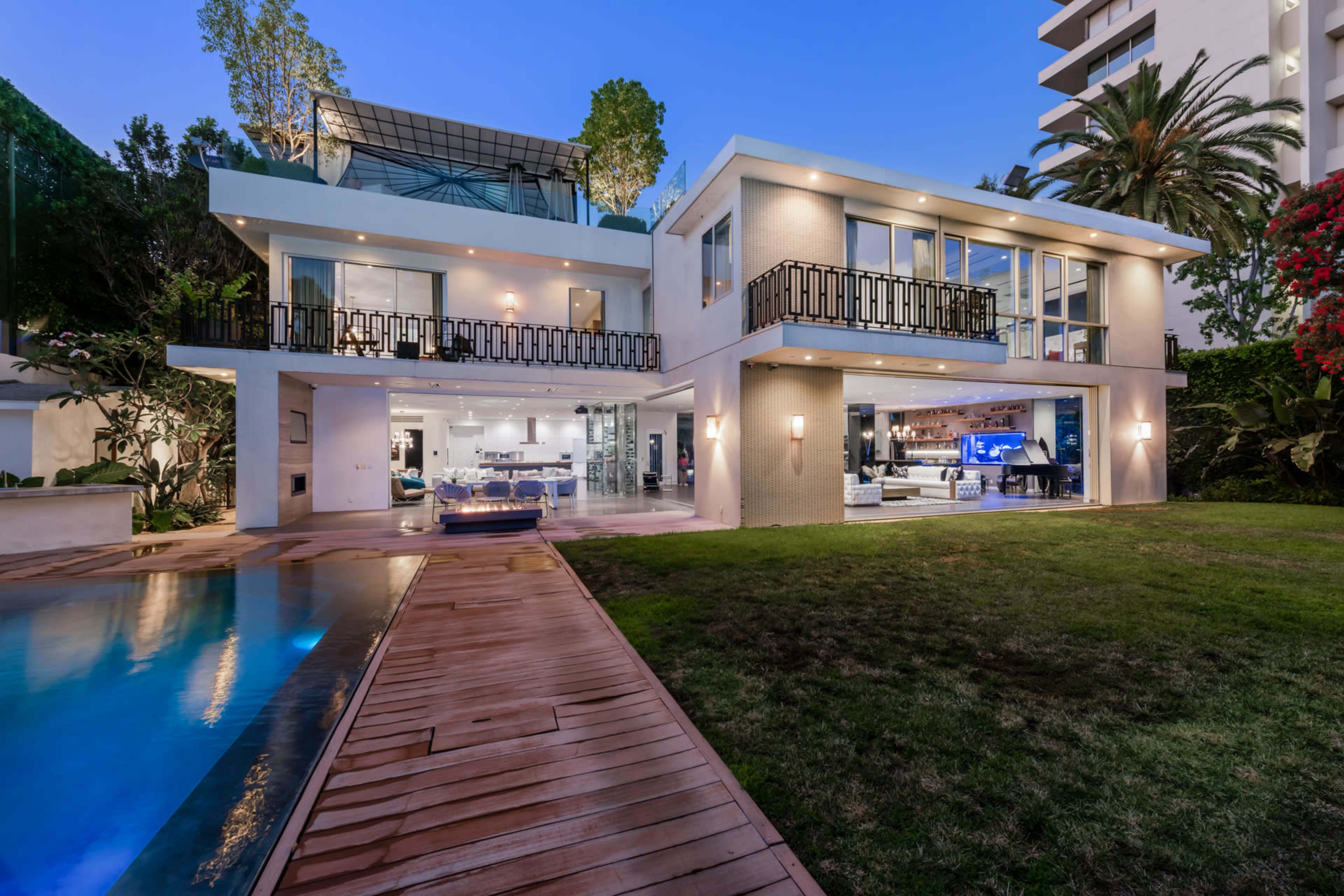 The image shows a modern two-story house with large windows, a swimming pool, and a well-maintained lawn.