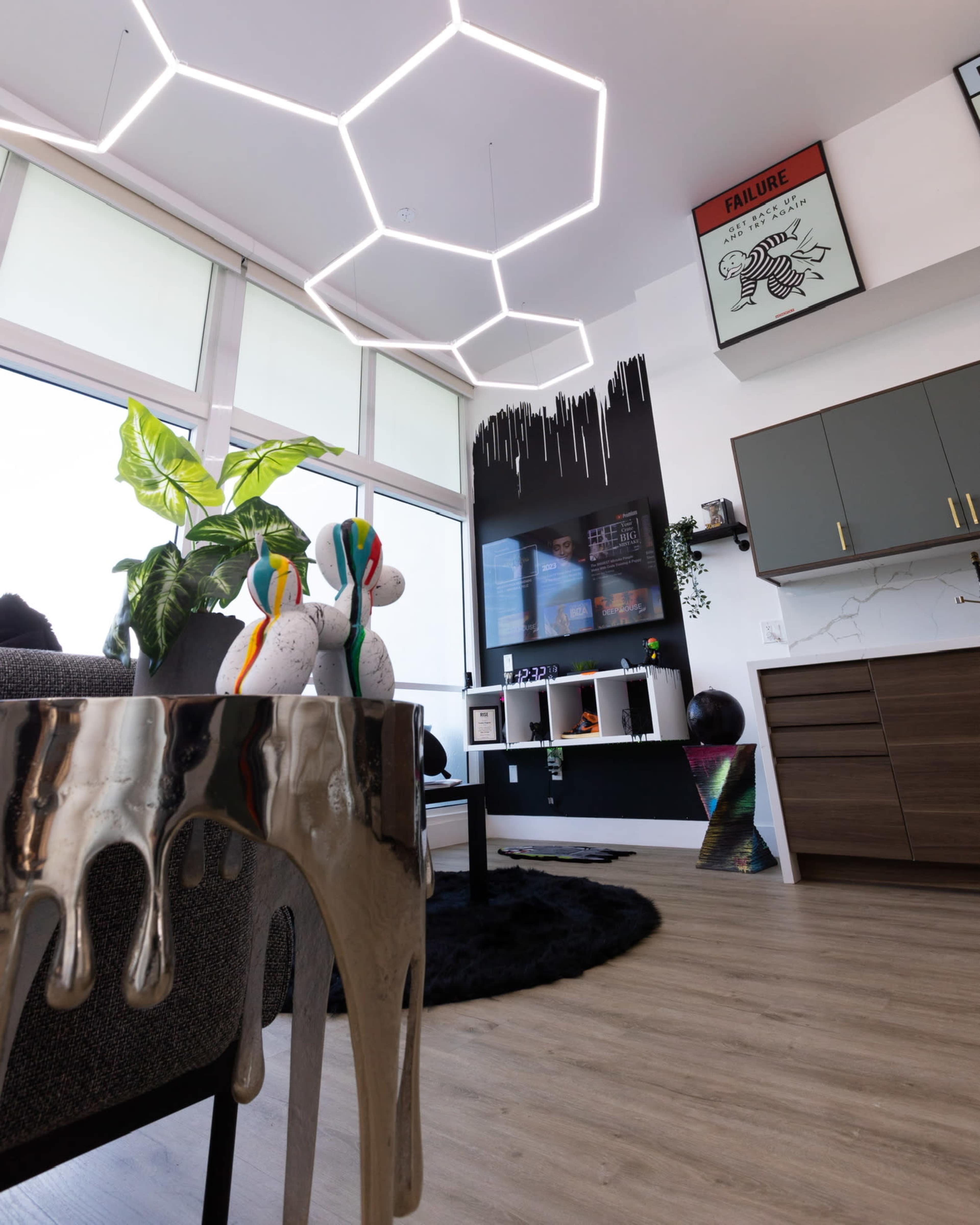 A modern living space featuring a hexagonal light fixture, a green plant, and decorative elements on the walls and shelves.