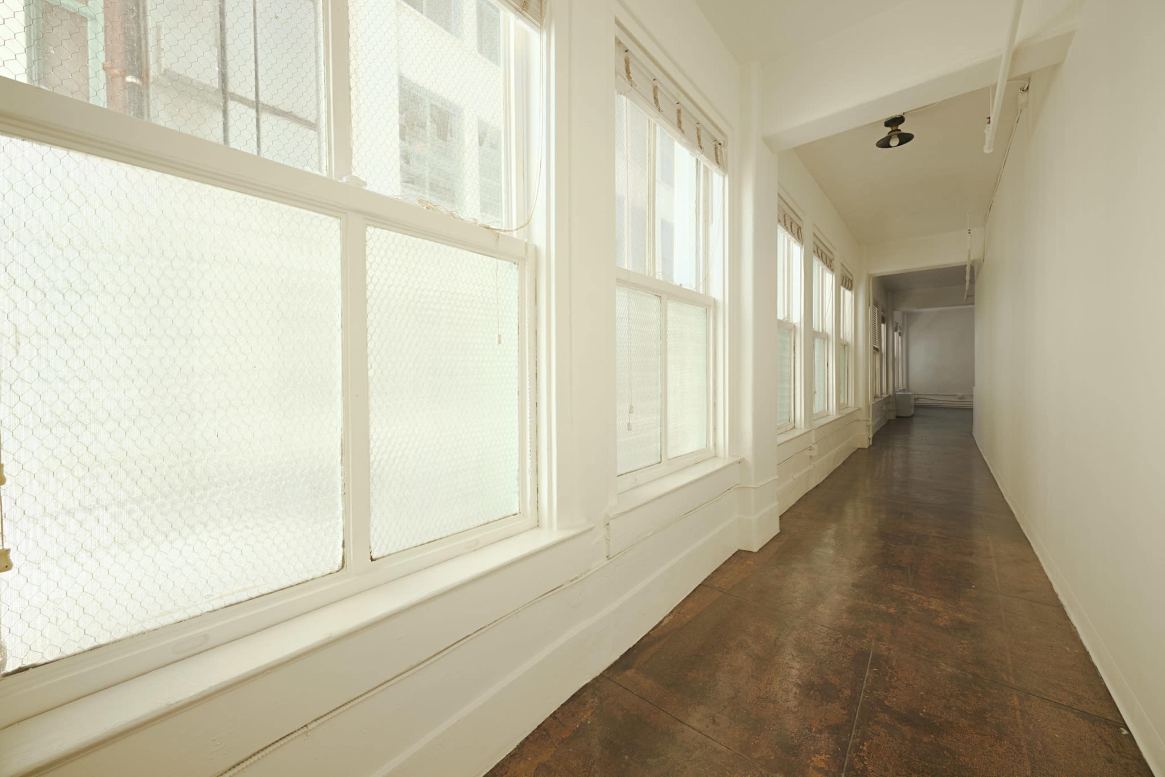 A long, narrow corridor with large windows along one side and a plain, white-painted wall on the other.
