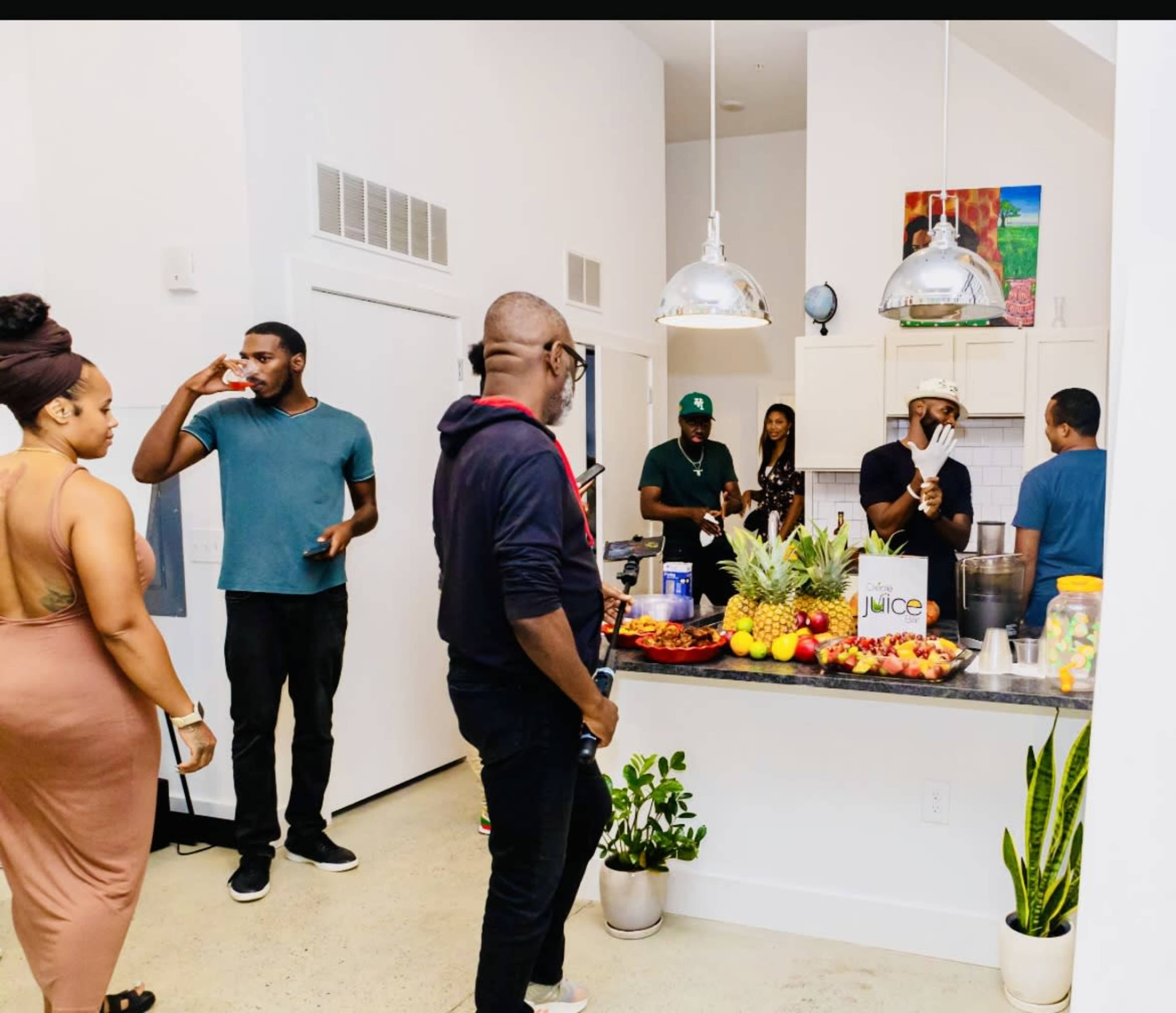 A group of people gathers in a modern kitchen featuring a variety of fresh fruits and a juice bar setup.
