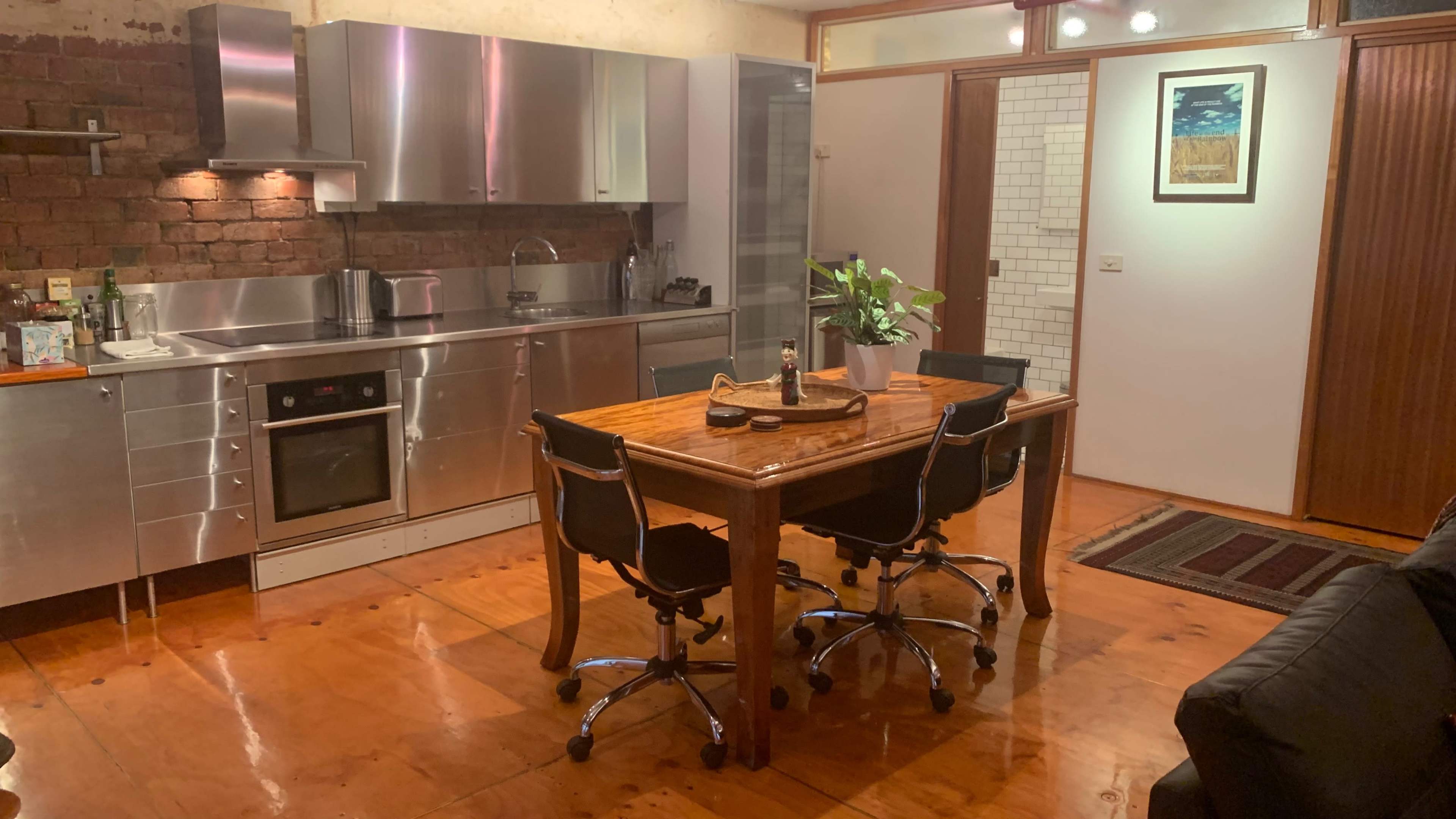 A modern kitchen with stainless steel appliances and a wooden dining table in the center, surrounded by black chairs.