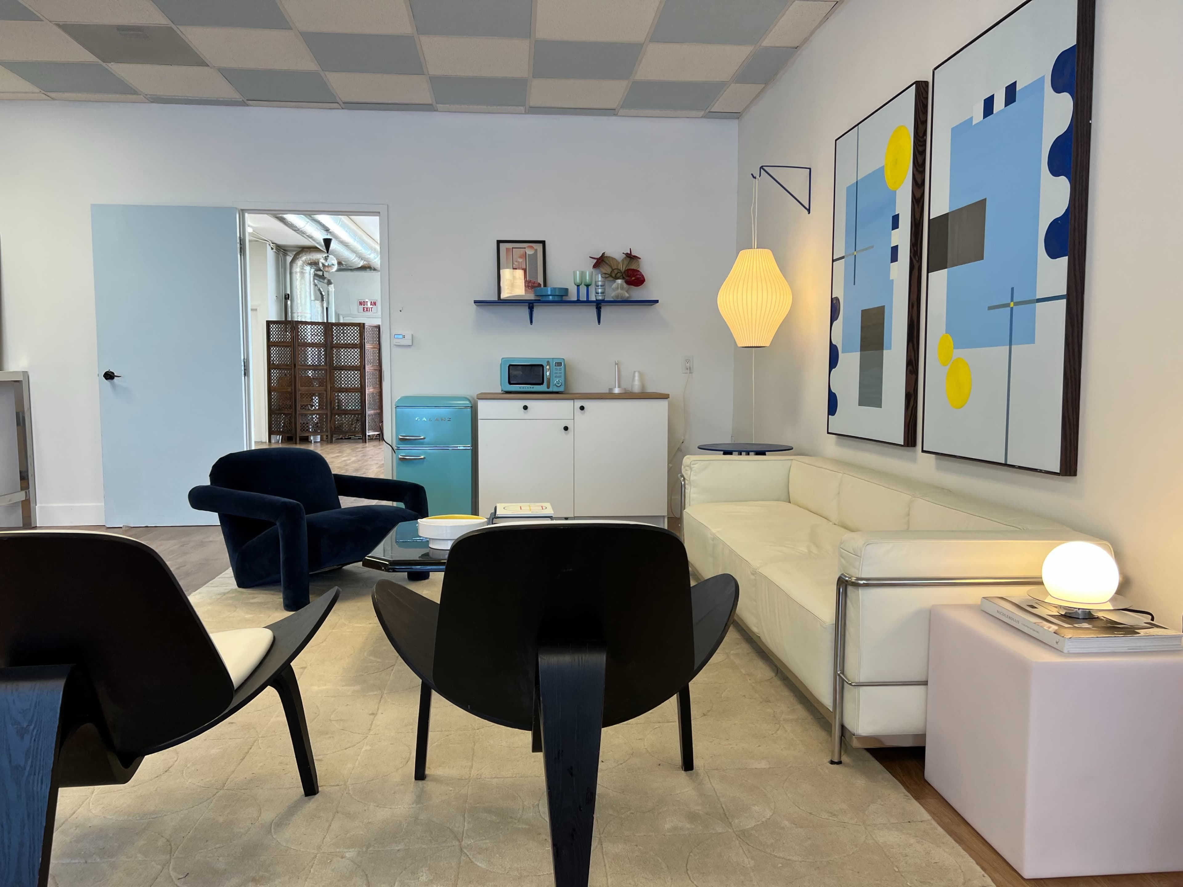 A modern, minimalist living room with a white sectional sofa, two black chairs, and abstract art on the walls.