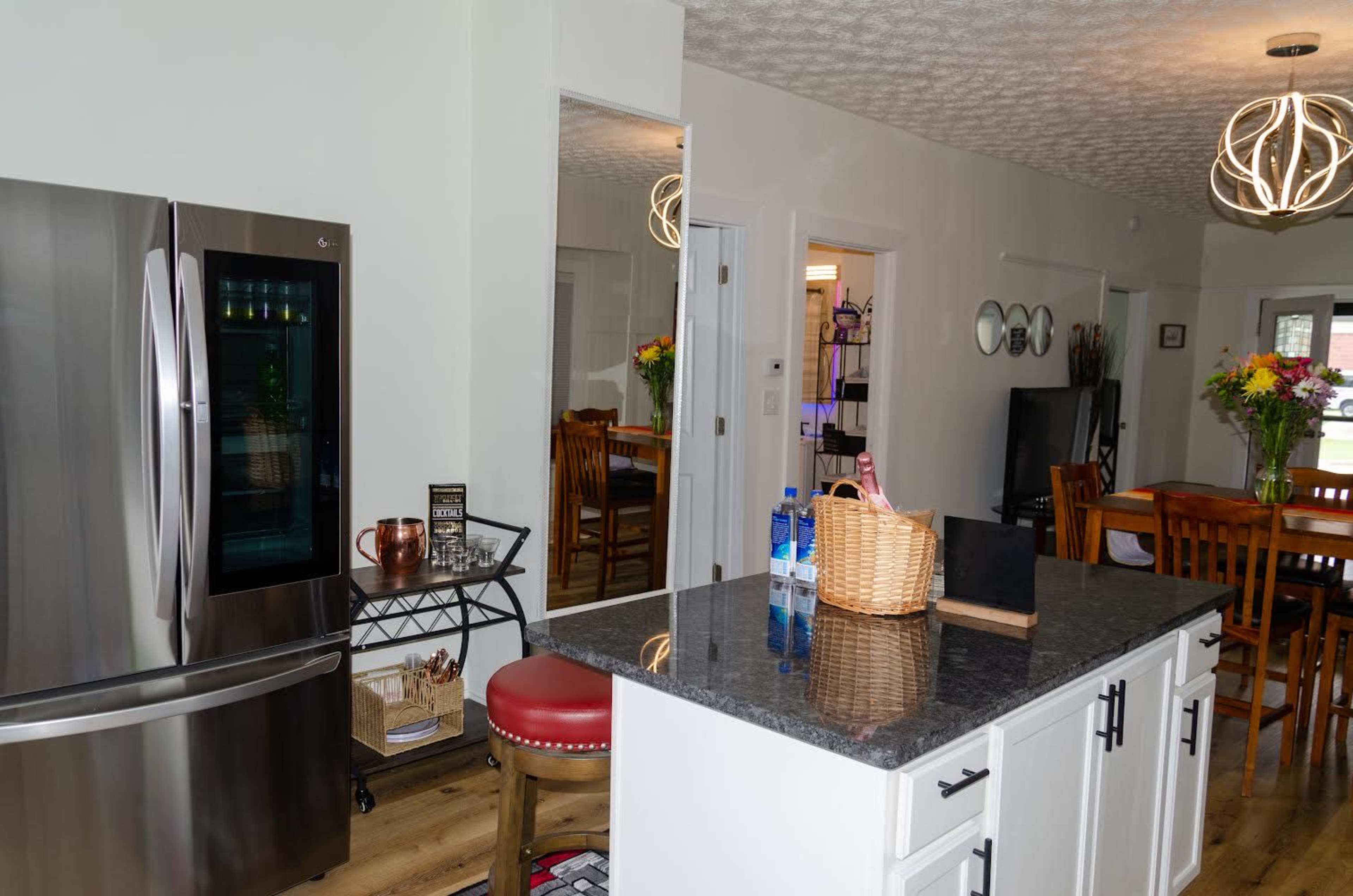 The kitchen features a stainless steel refrigerator, an island with a dark countertop, and a dining area with wooden chairs and a table.