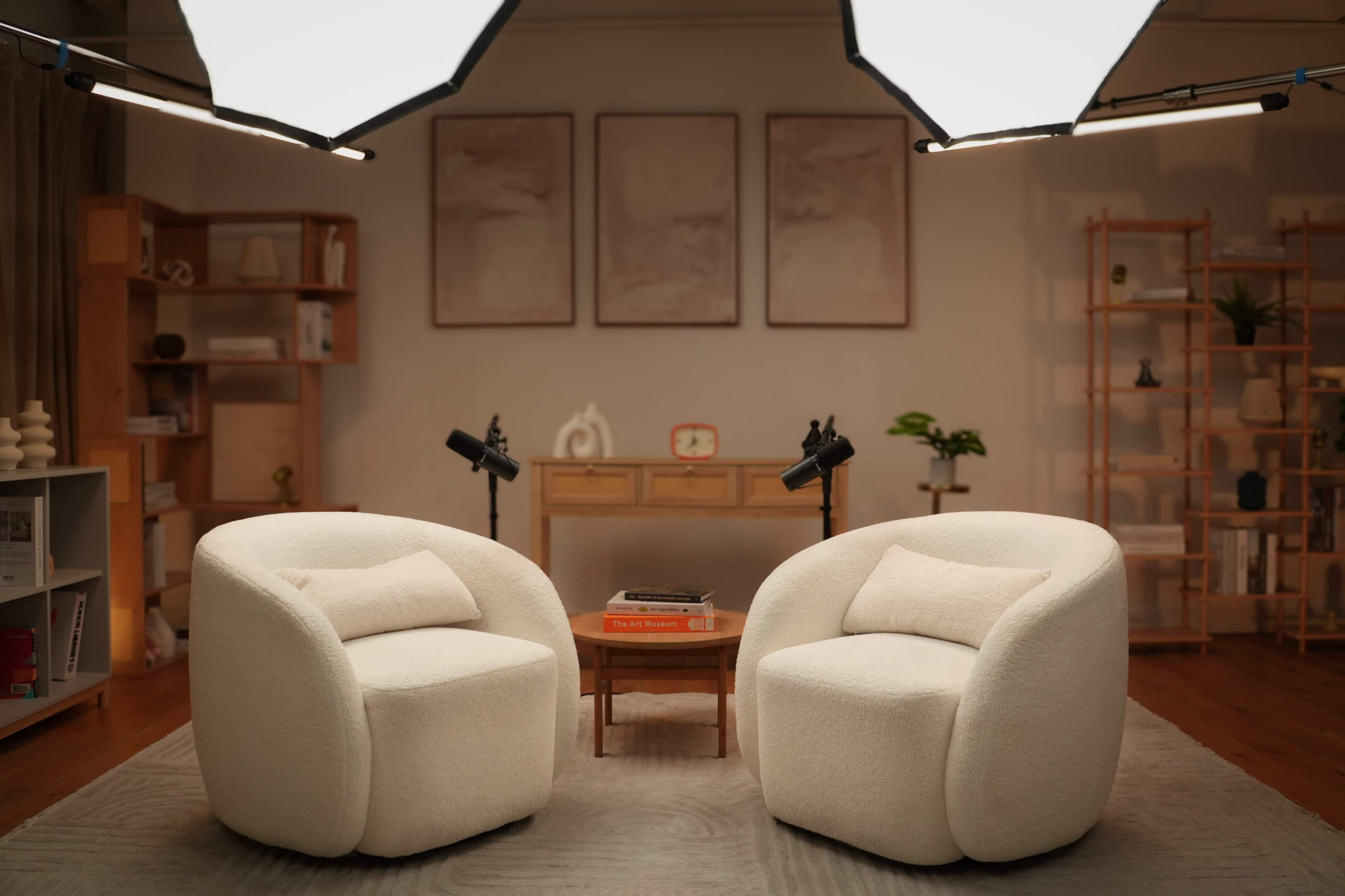 The scene features two cozy, white armchairs positioned around a small wooden table in a well-lit, minimalist living room with decorative shelves and framed art on the walls.