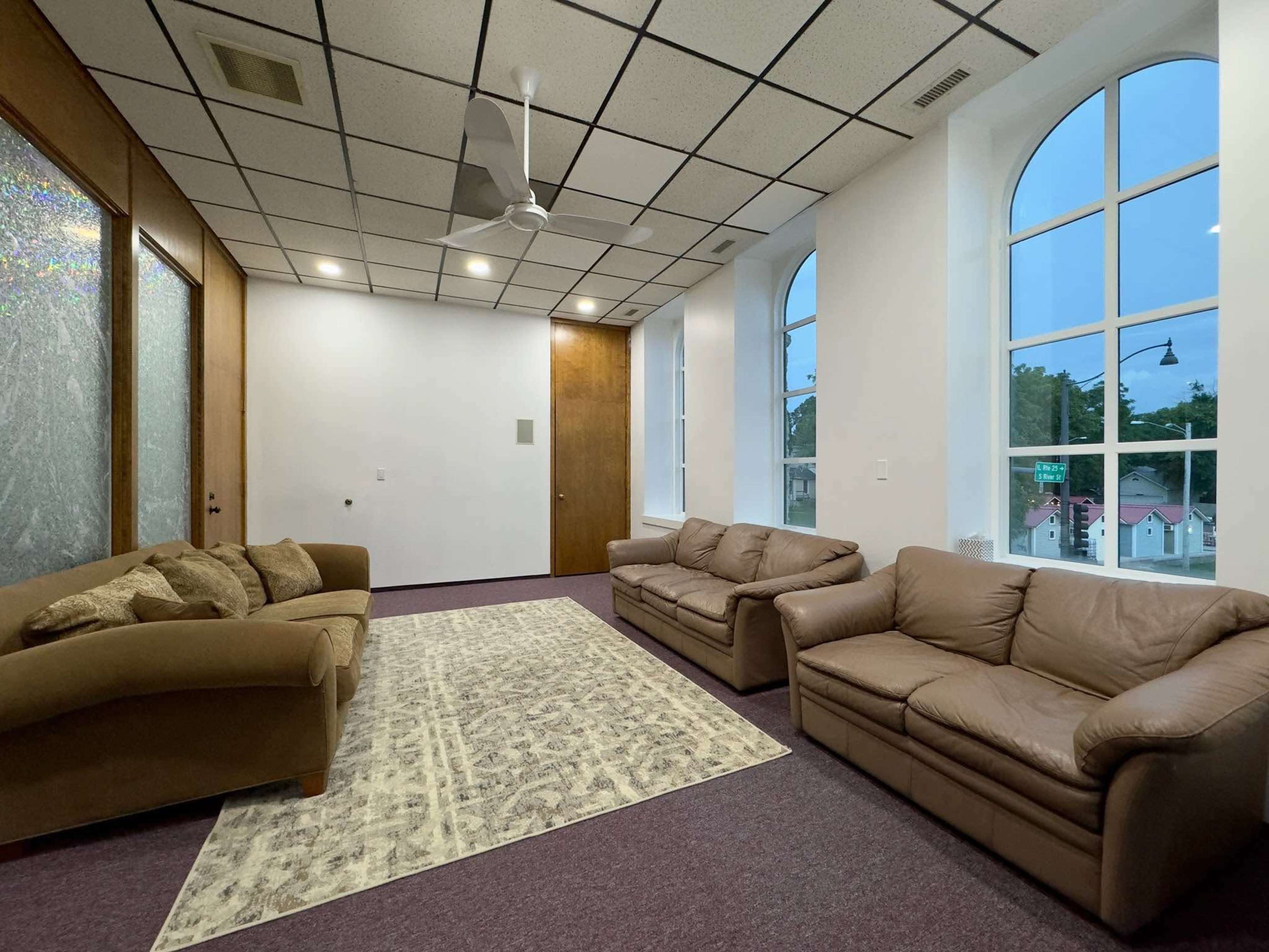 A spacious room with two brown leather sofas, a light-colored area rug, and large windows that let in natural light.