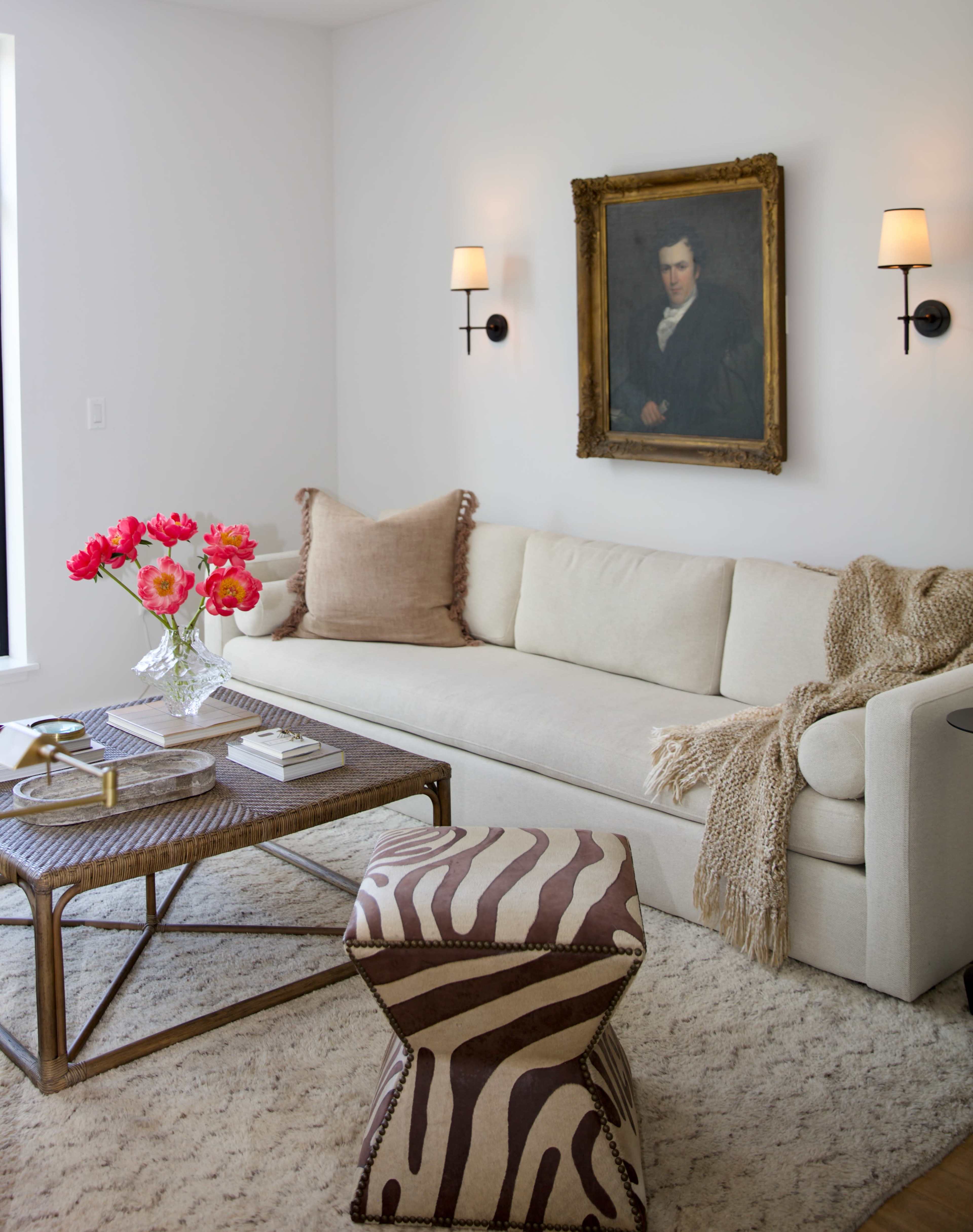 A modern living room features a light-colored sofa, a zebra-striped ottoman, and a floral centerpiece on a coffee table, with a portrait on the wall.