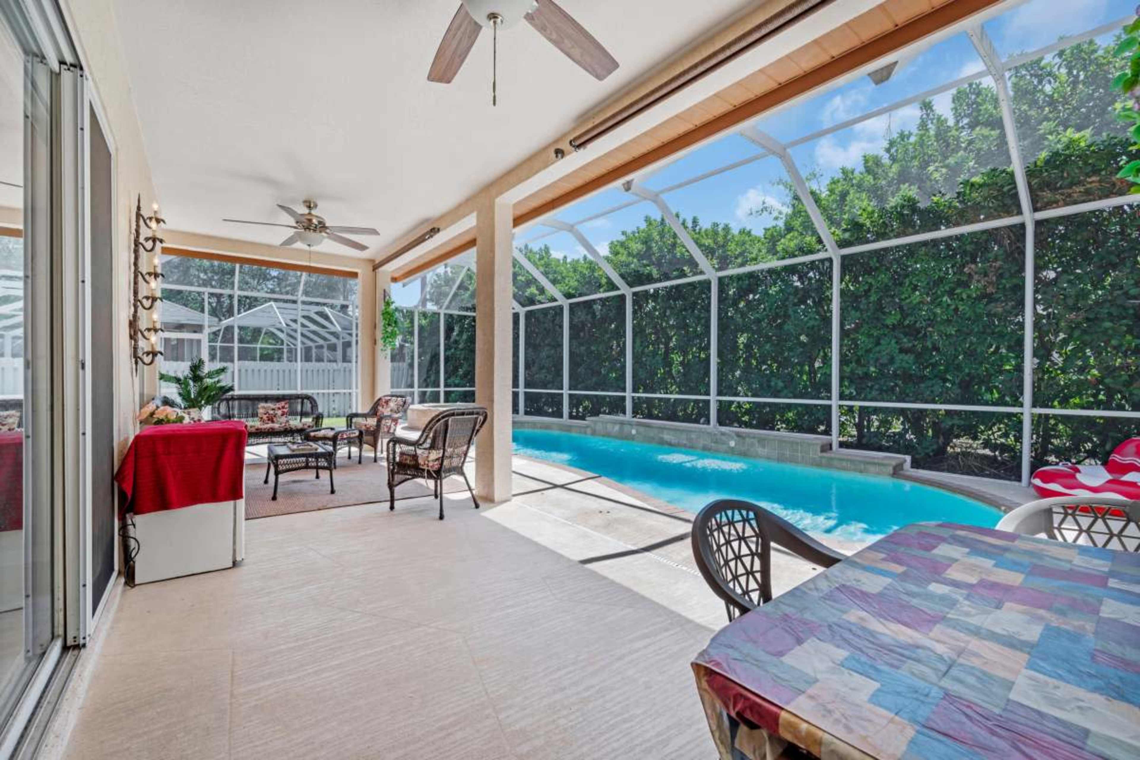 The image shows a screened patio area with a seating arrangement and a swimming pool visible beyond it.