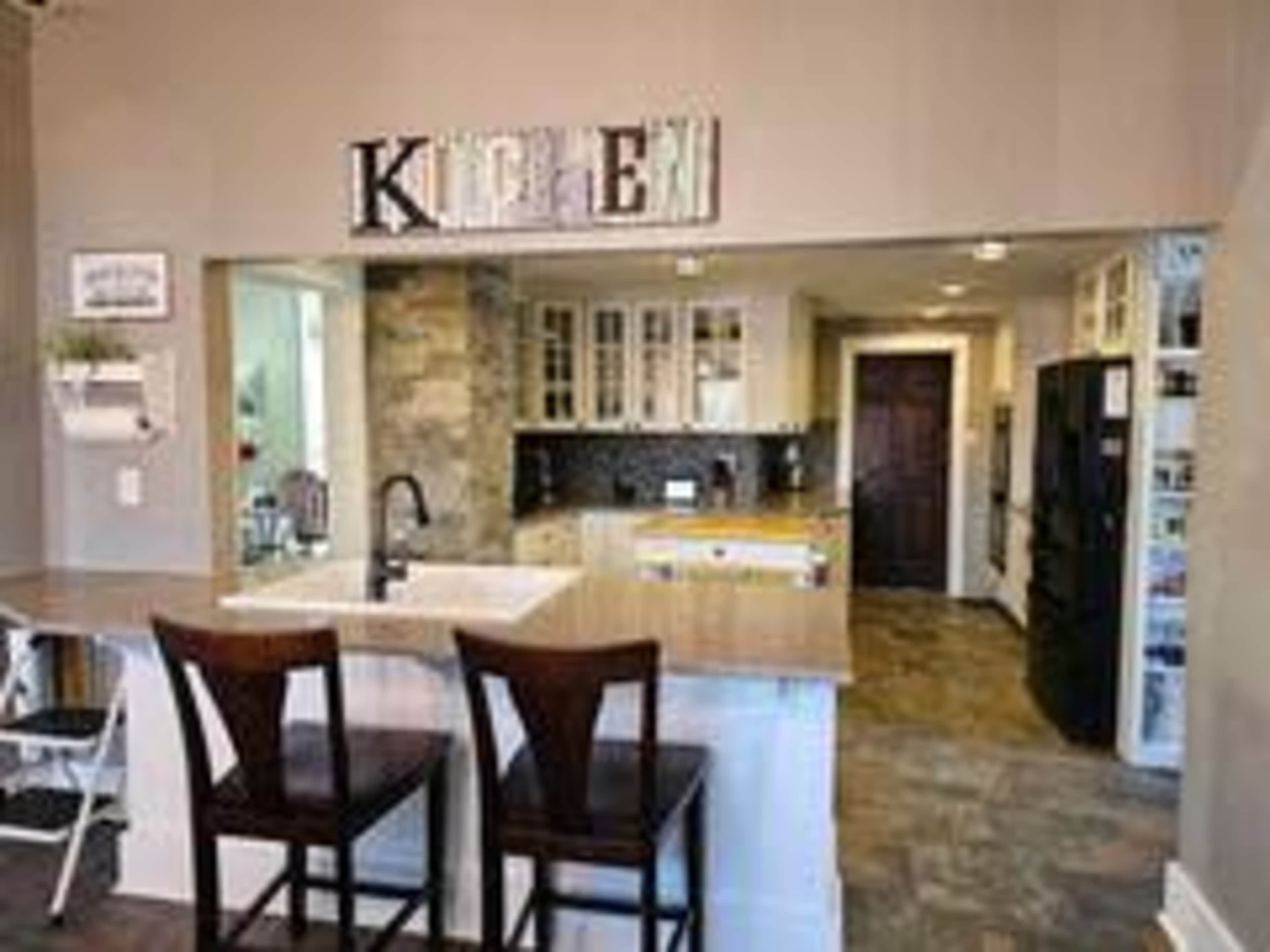 A modern kitchen features a stone accent wall, wooden bar counter with two stools, and cabinets displaying both glass and solid doors.