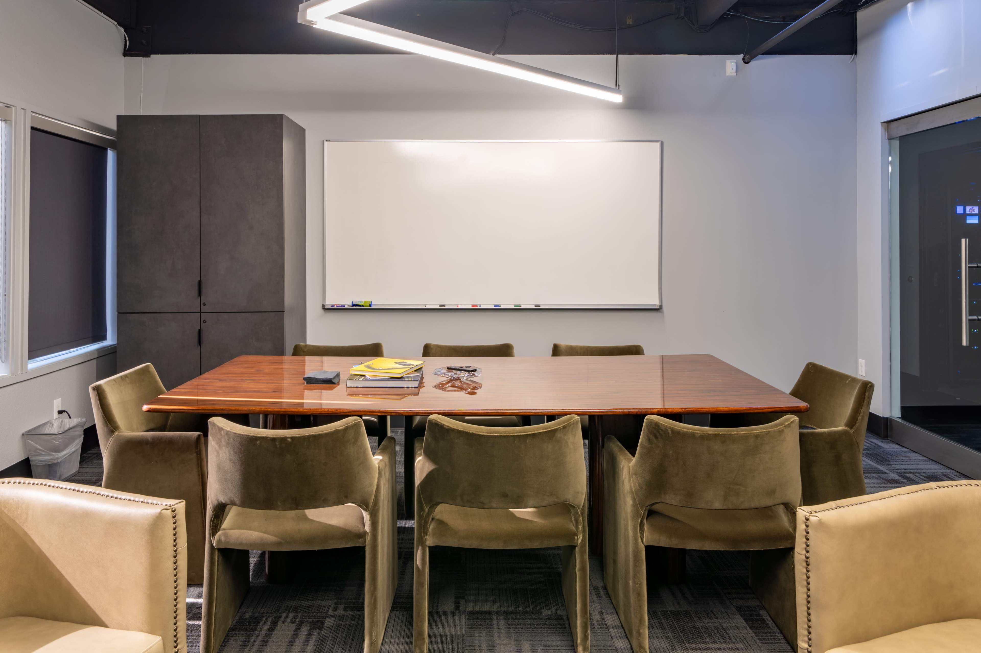 A modern conference room features a large wooden table surrounded by eight green chairs and a whiteboard on the wall.