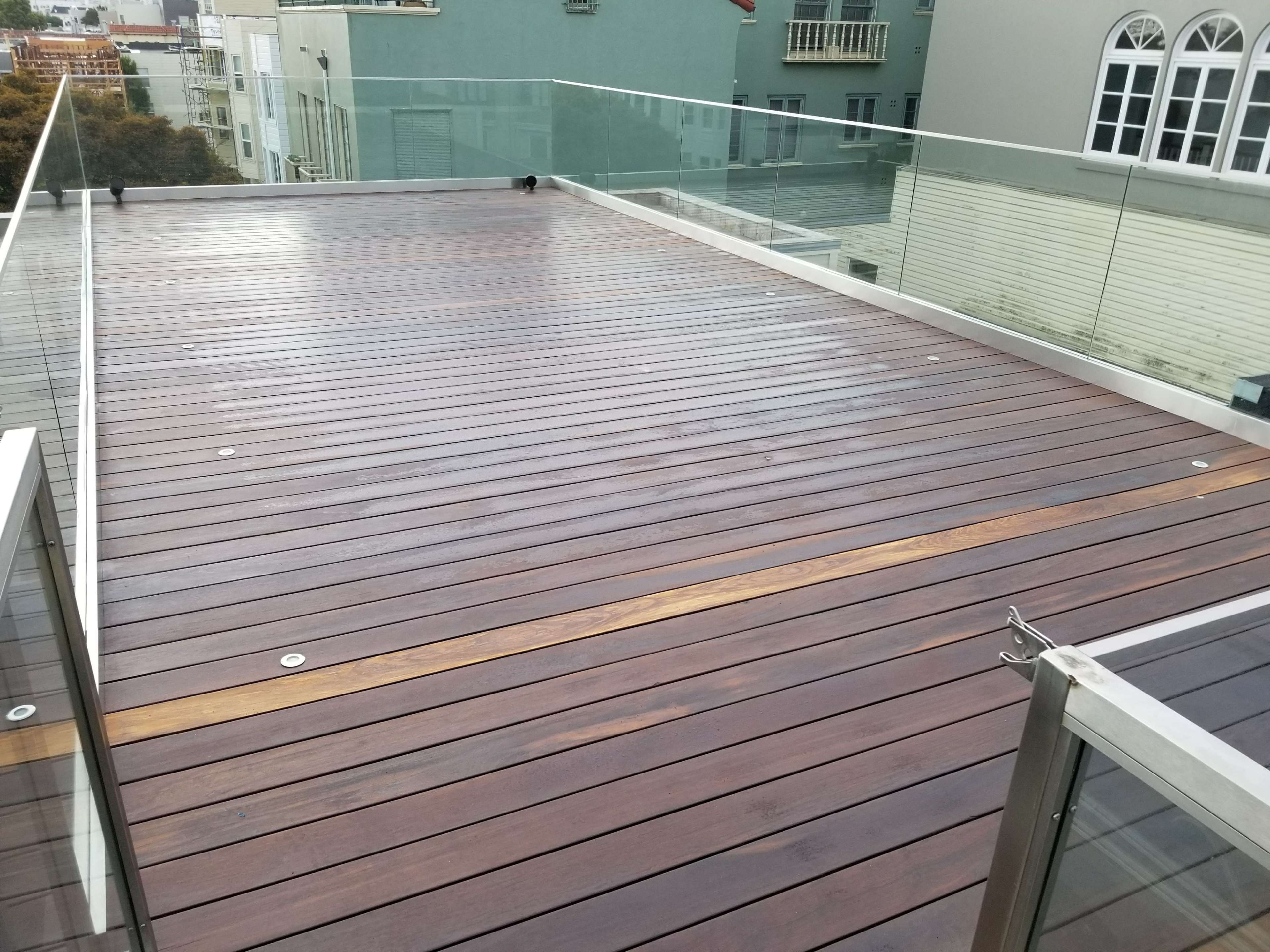 A wooden deck with a smooth surface and glass railing in an urban setting.