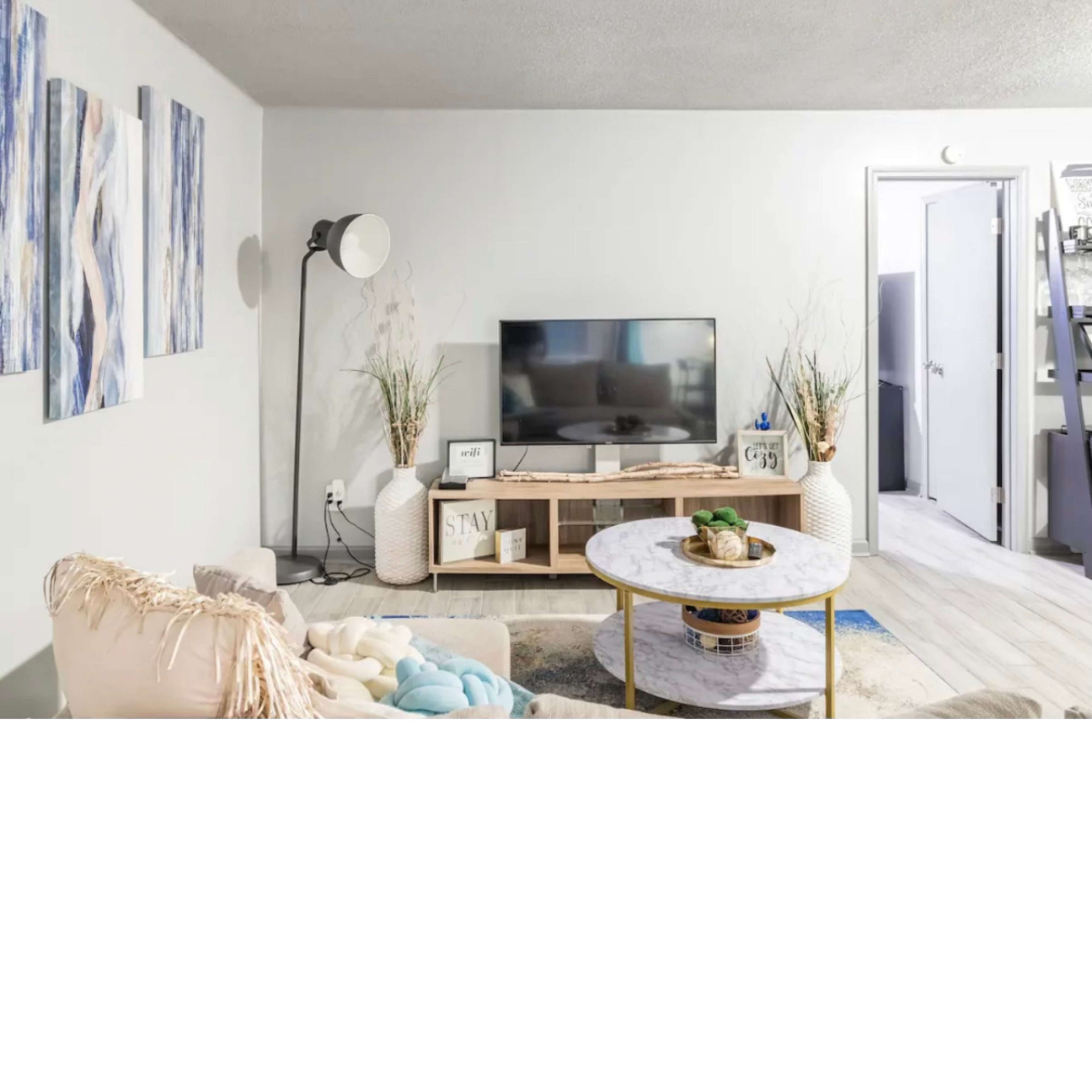 The living room features a television on a wooden stand, a round coffee table with decor items, and abstract art on the walls.