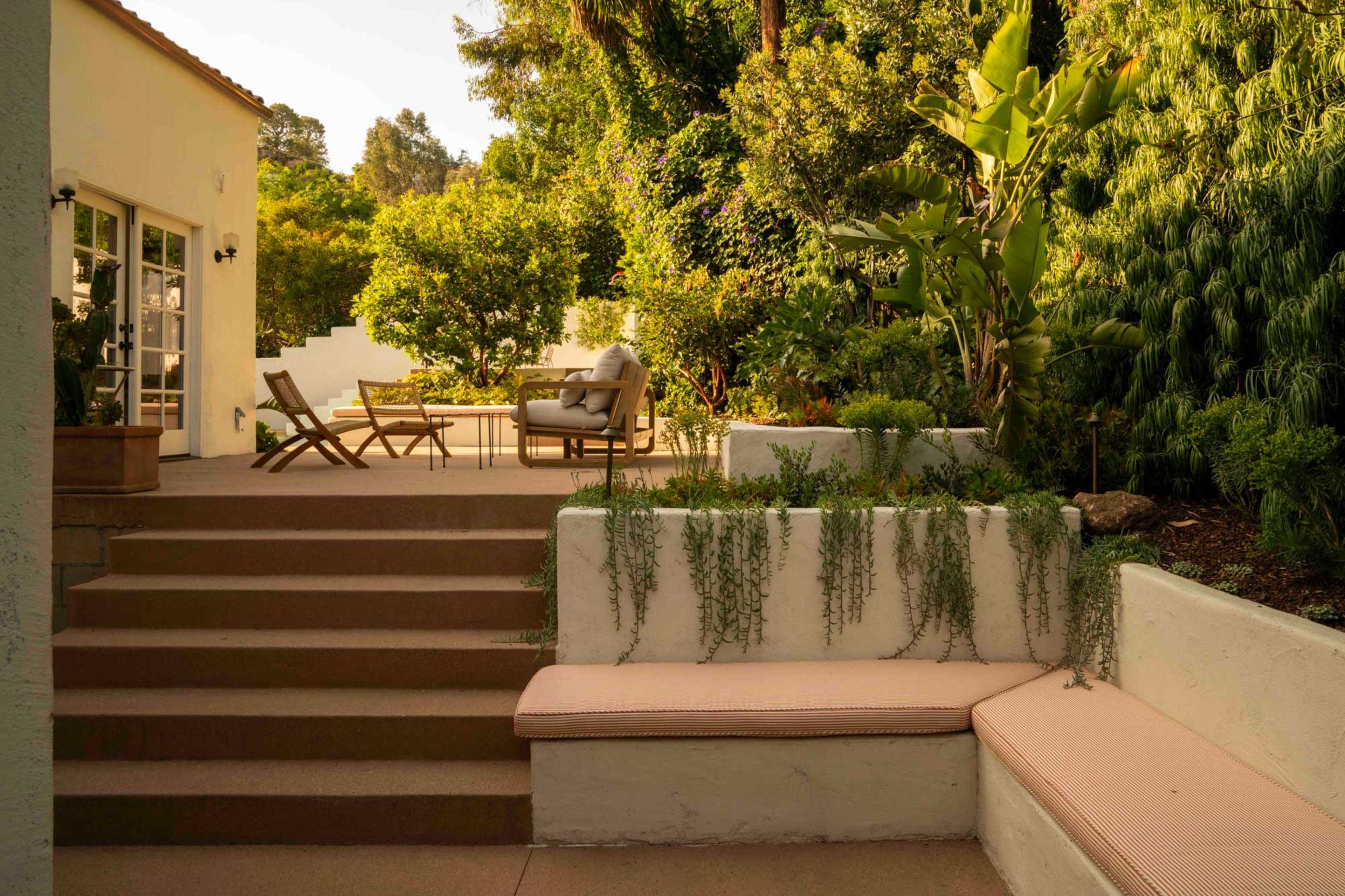 The image shows a landscaped outdoor patio with steps leading to seating areas surrounded by greenery.