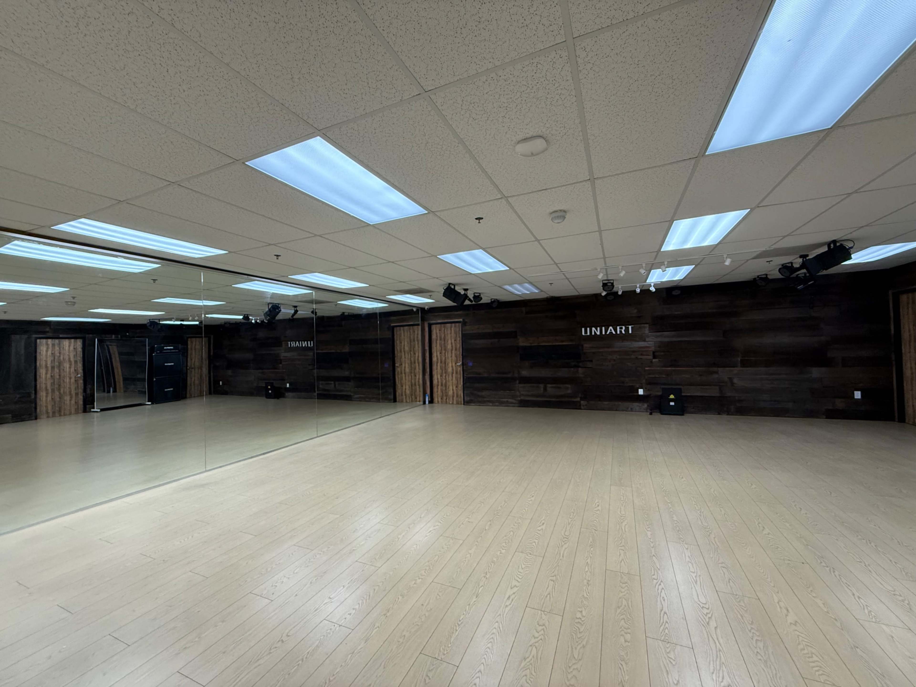 The image shows a spacious dance studio with wooden flooring, mirrored walls, and a dark wood paneled background.