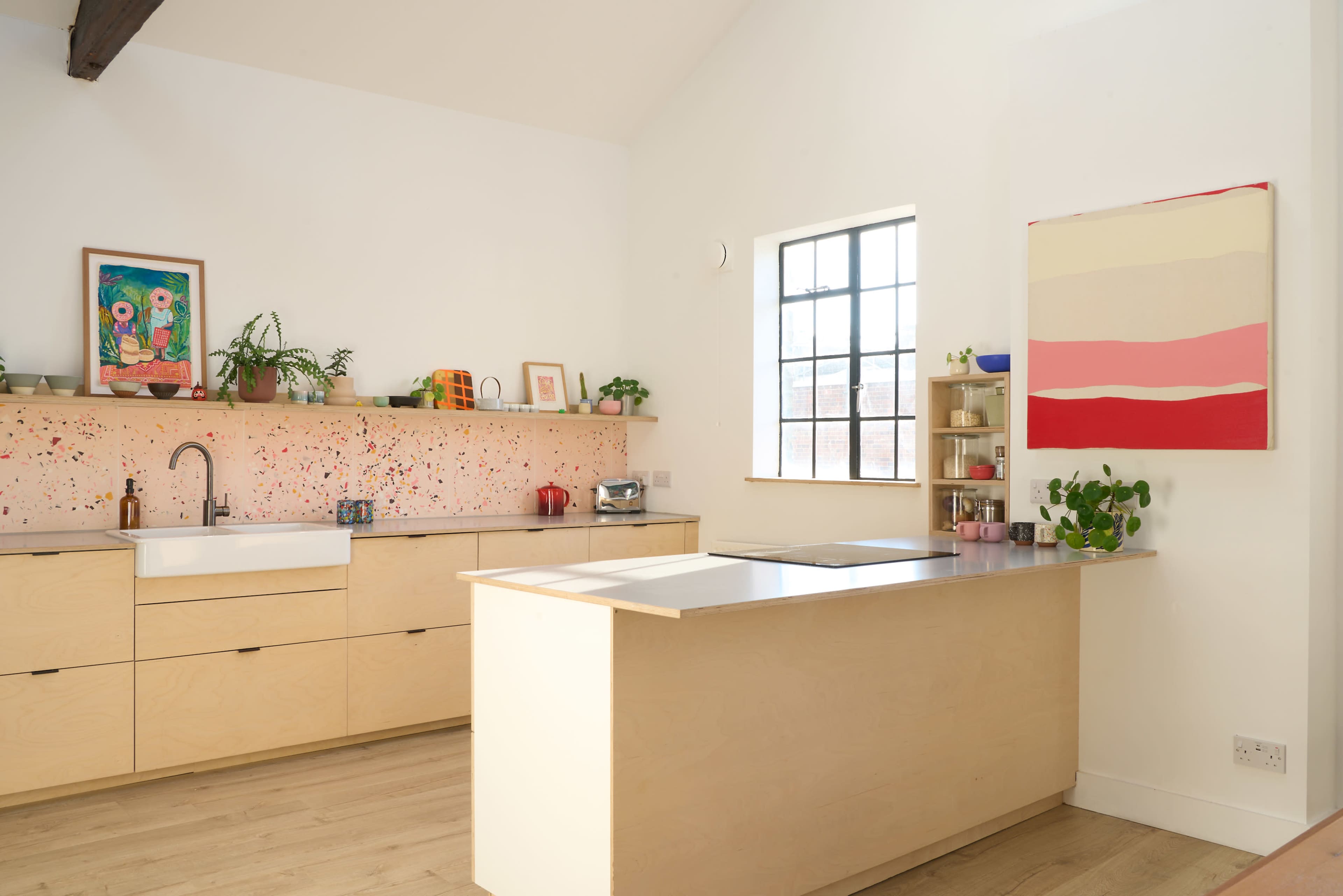 The image shows a modern kitchen with light wood cabinetry, a large sink, and a colorful backsplash featuring splashes of various colors.