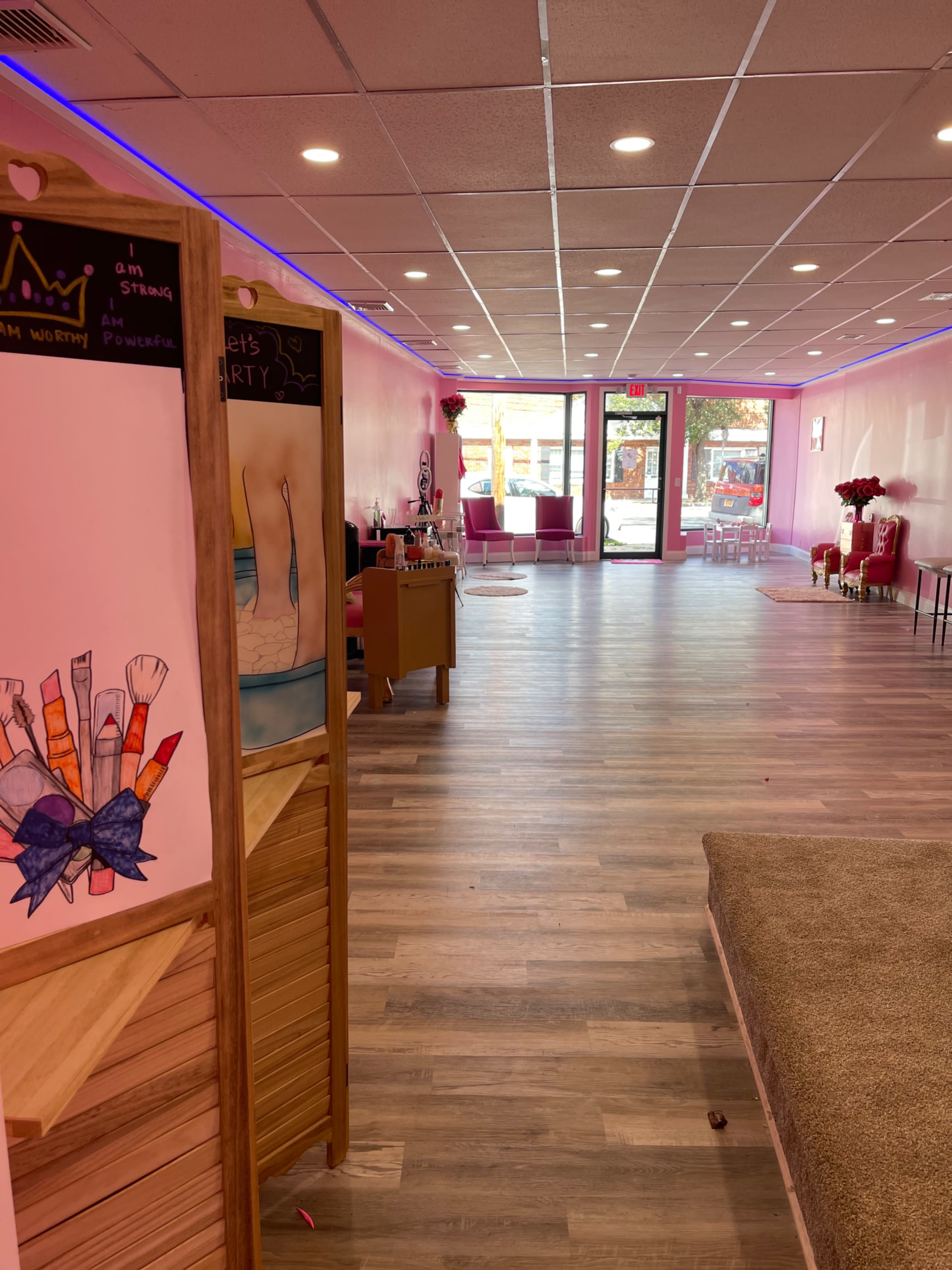 A brightly colored, empty beauty salon with pink walls and a wooden divider with decorative artwork.