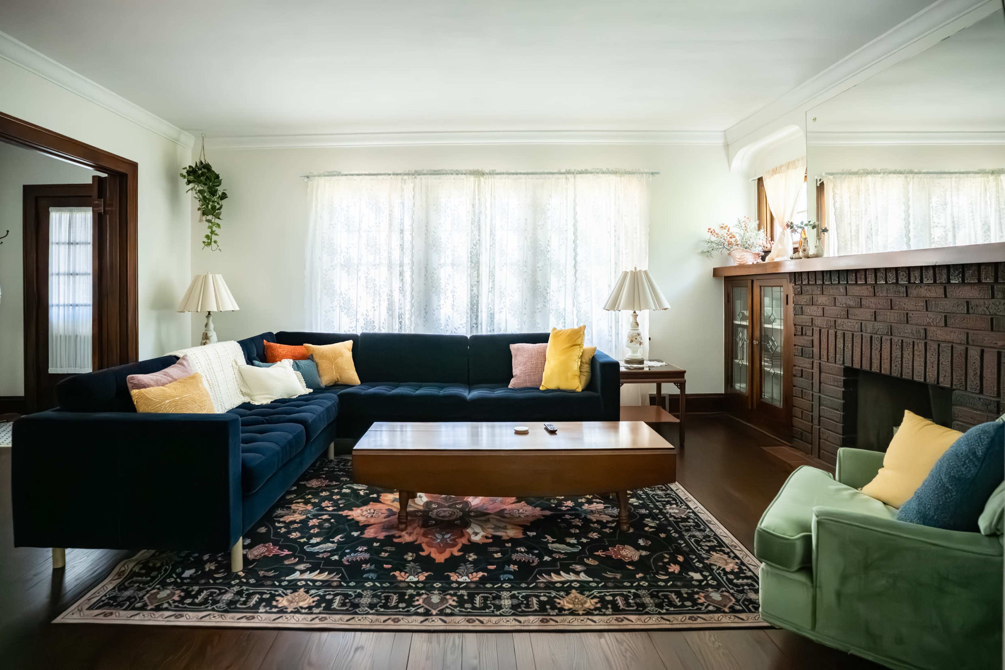 The living room features a dark blue sectional sofa, a wooden coffee table, and a vintage-style rug, with large windows allowing natural light to illuminate the space.