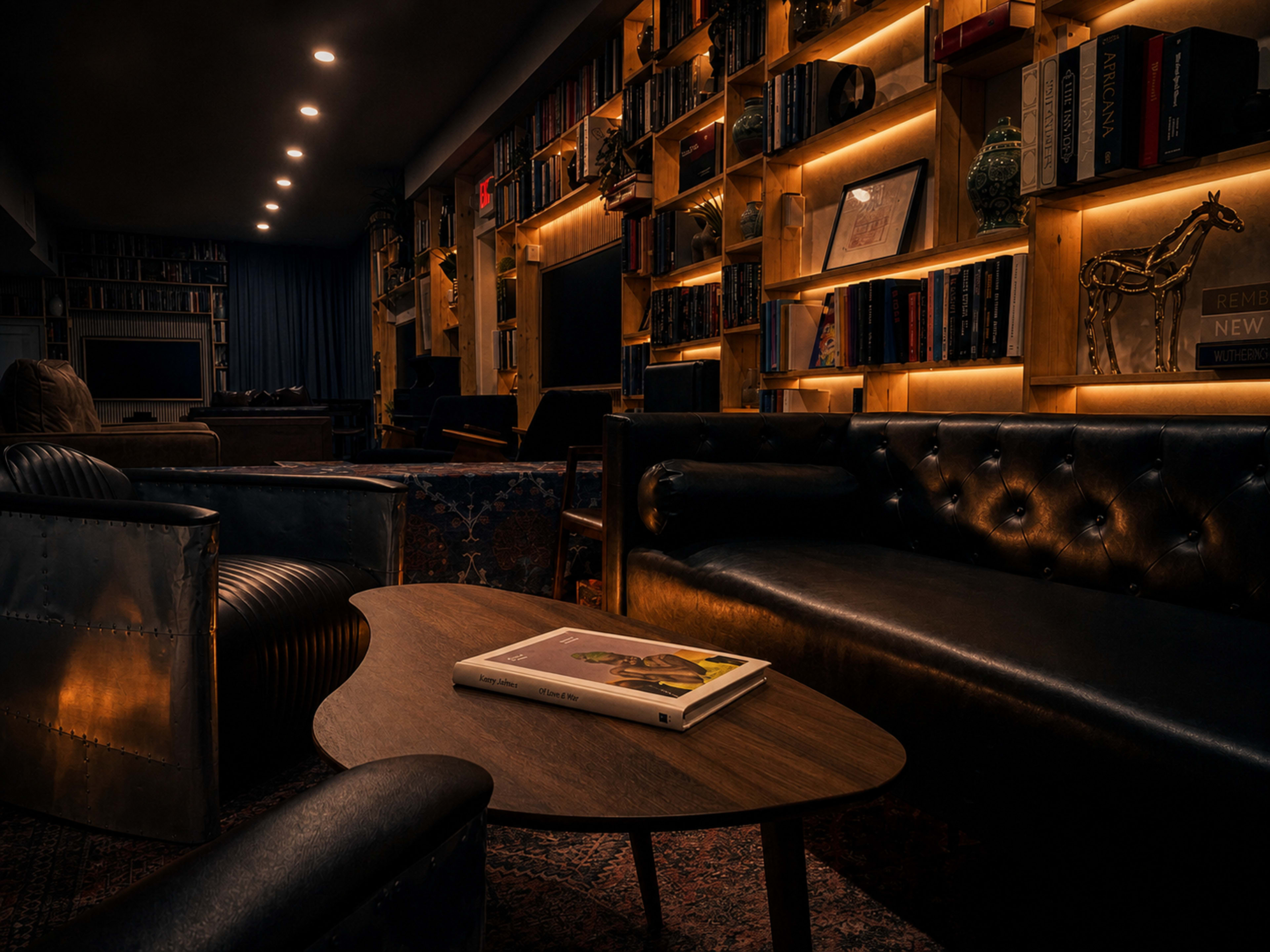 The image shows a cozy seating area with leather sofas and a wooden coffee table, surrounded by bookshelves filled with books and decorative items.