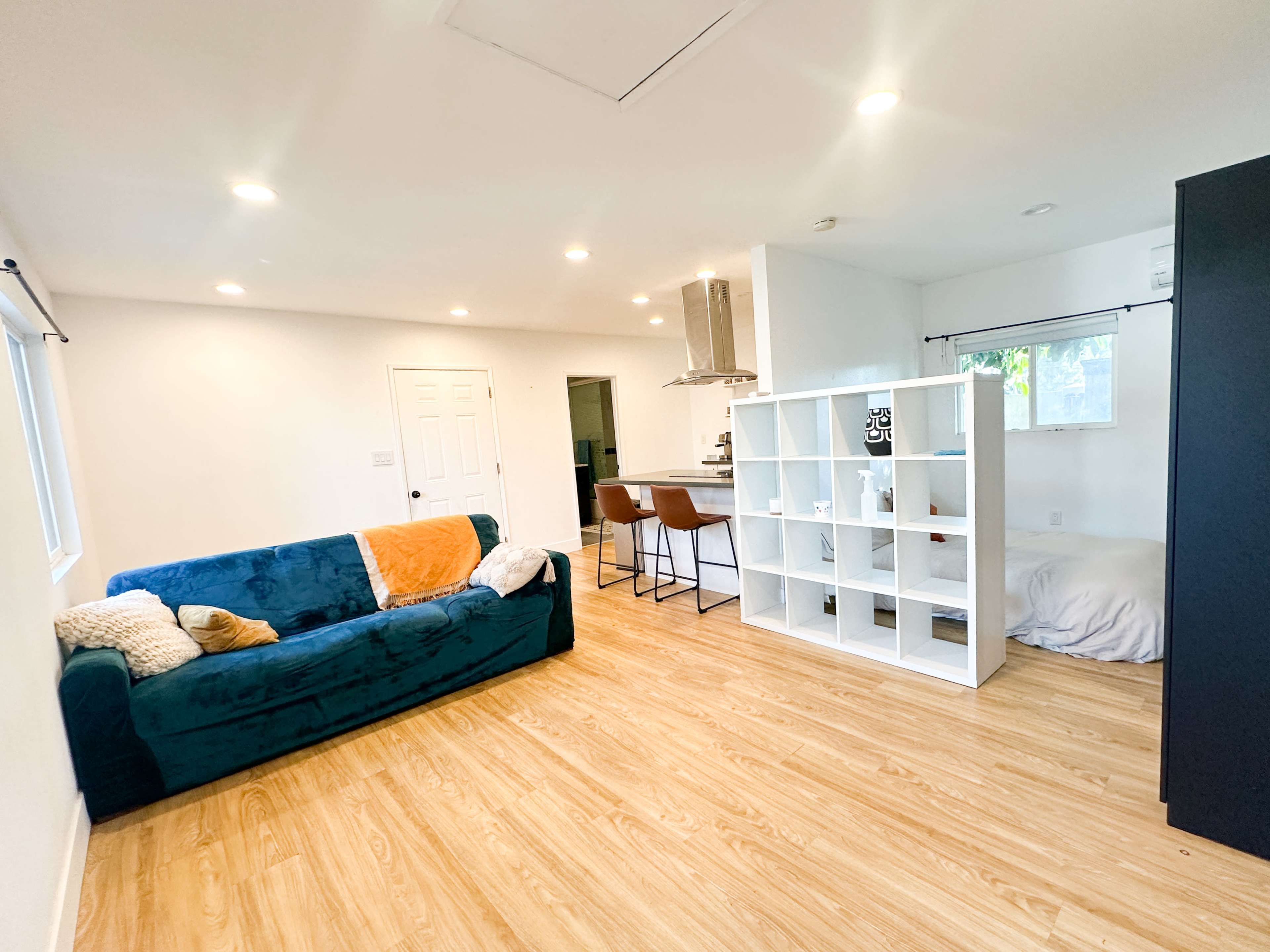 A modern living space with a teal couch, a shelving unit, and a kitchen area with bar seating.