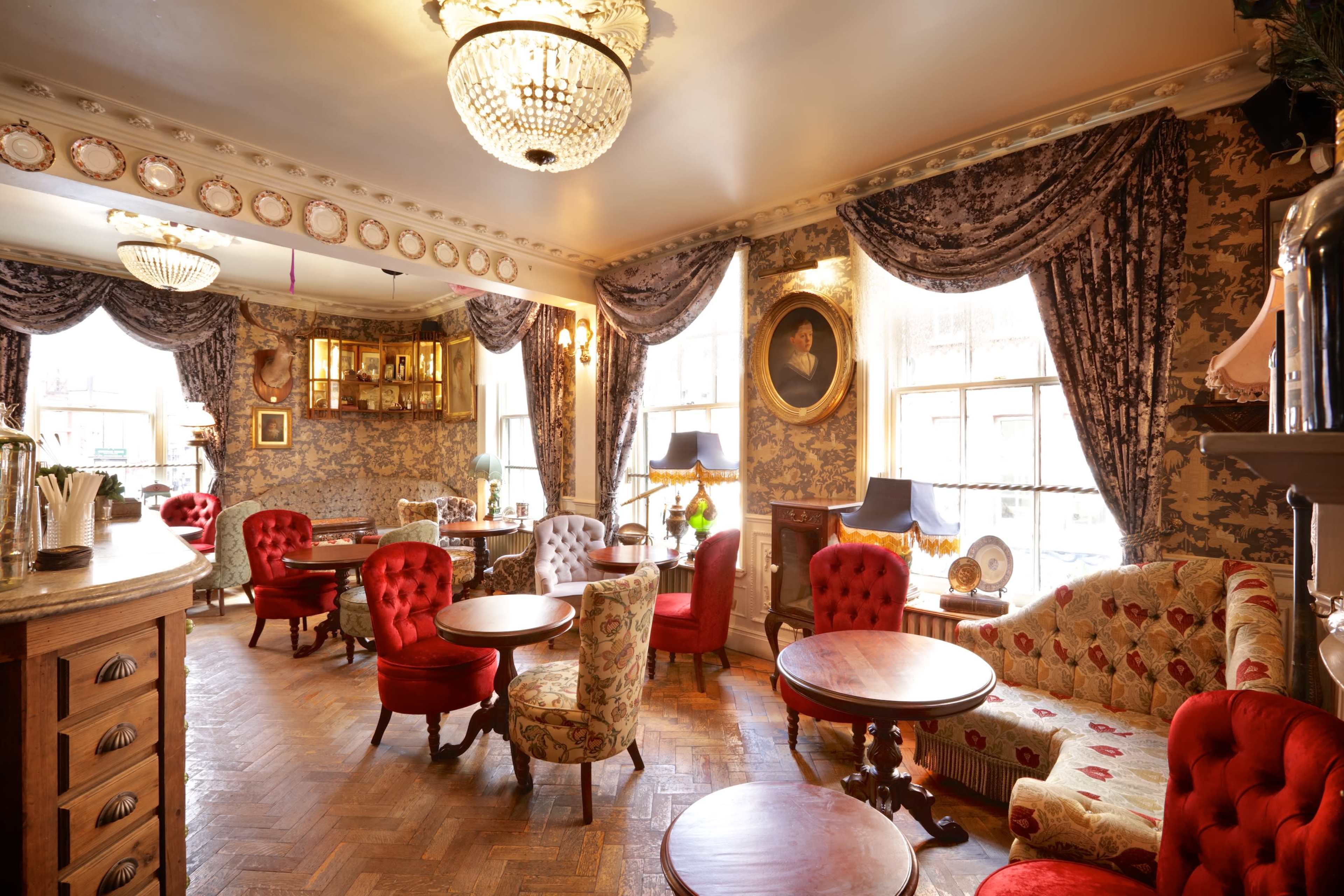 A cozy, elegantly decorated lounge area with patterned wallpaper, plush seating, and large windows allowing natural light.