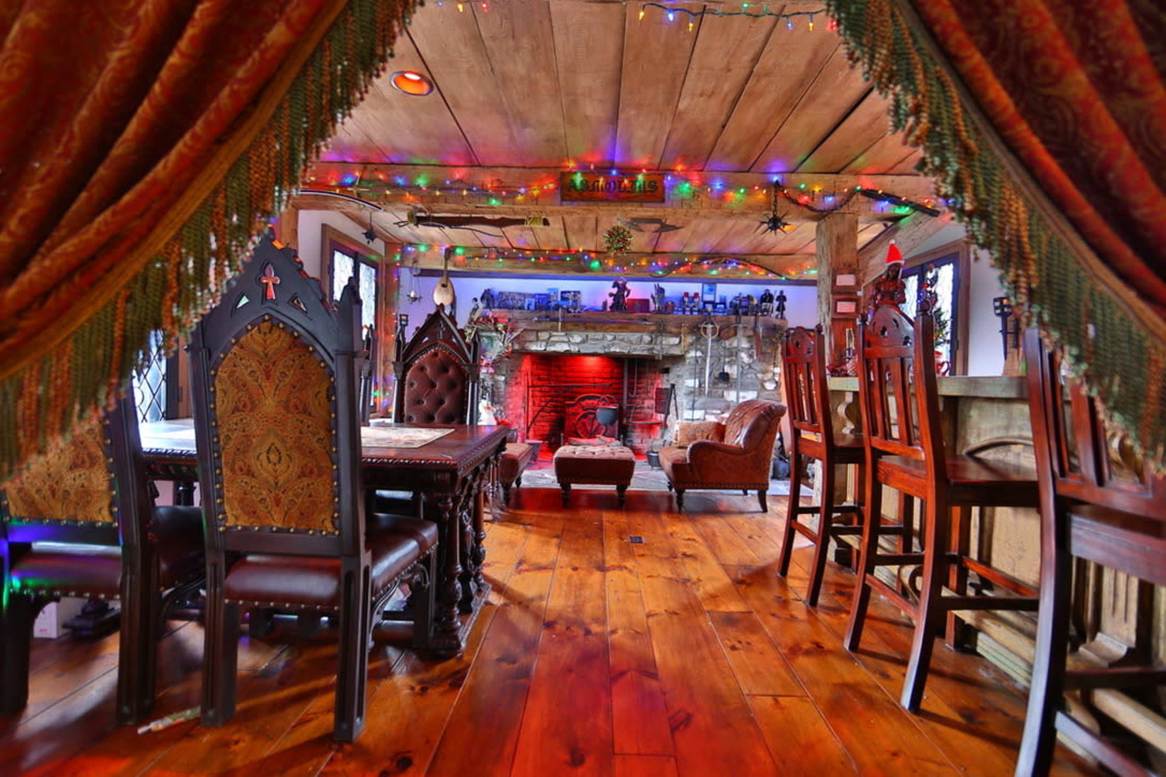 The image shows a cozy dining area with ornate chairs and a view of a stone fireplace, decorated with colorful lights and draped curtains.