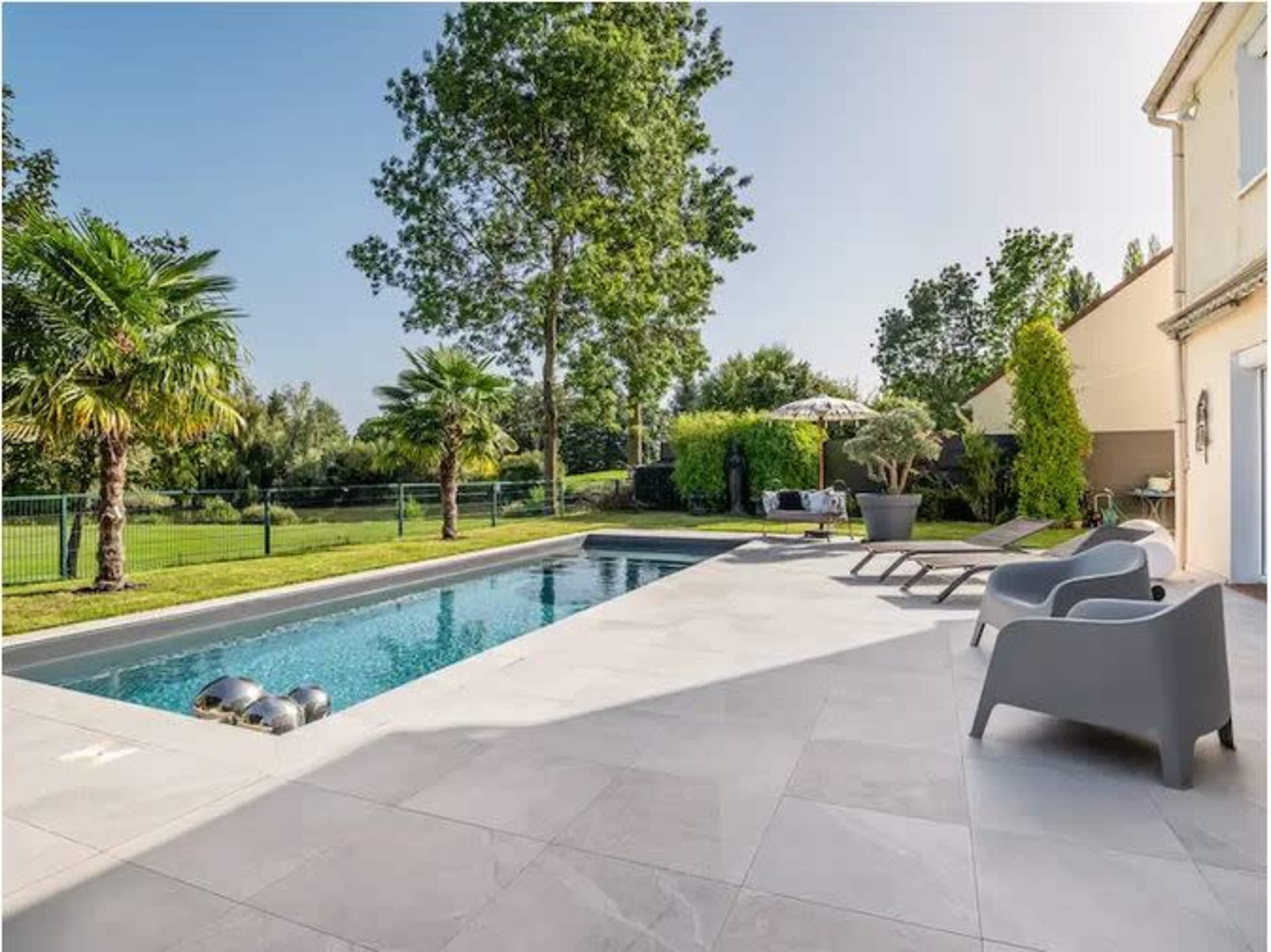 The image shows a modern residential backyard featuring a swimming pool surrounded by palm trees and patio furniture.