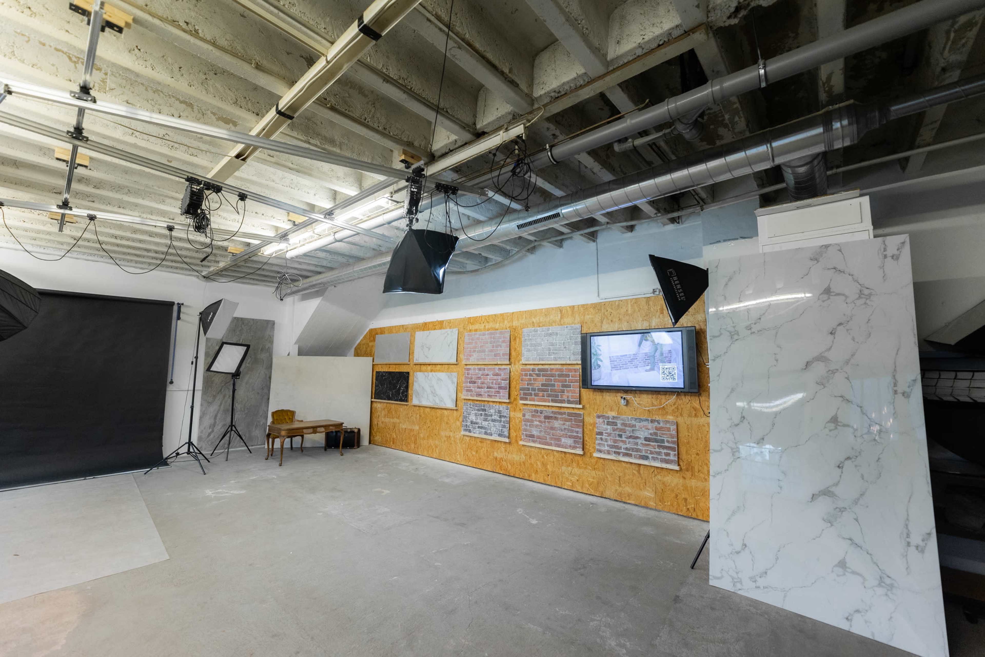 The room features a display of various wall materials, including brick and marble, with lighting and a television screen along one side.