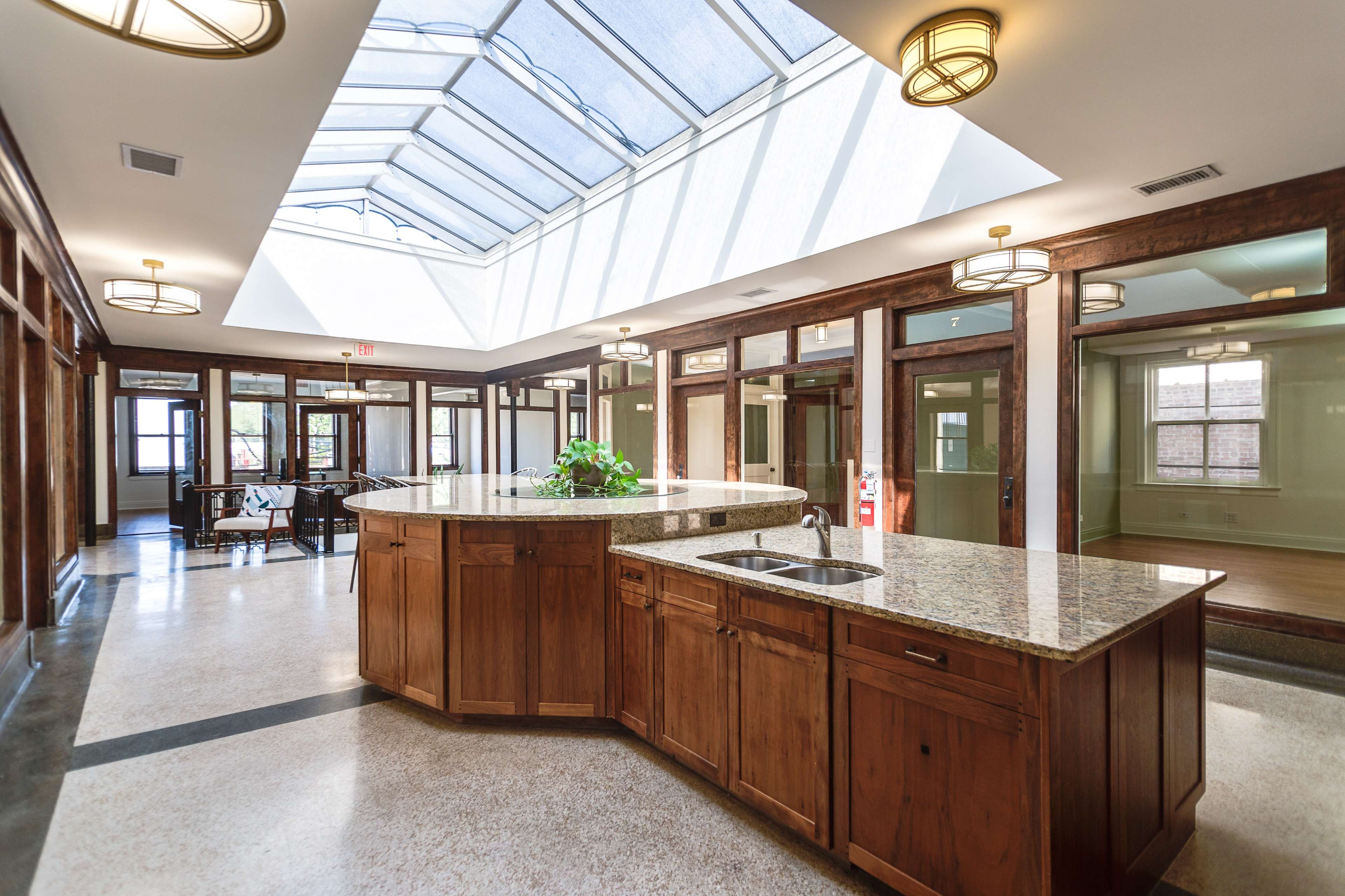 A spacious kitchen area with a central island made of wood and granite, under a skylight, surrounded by wooden doors leading to other rooms.