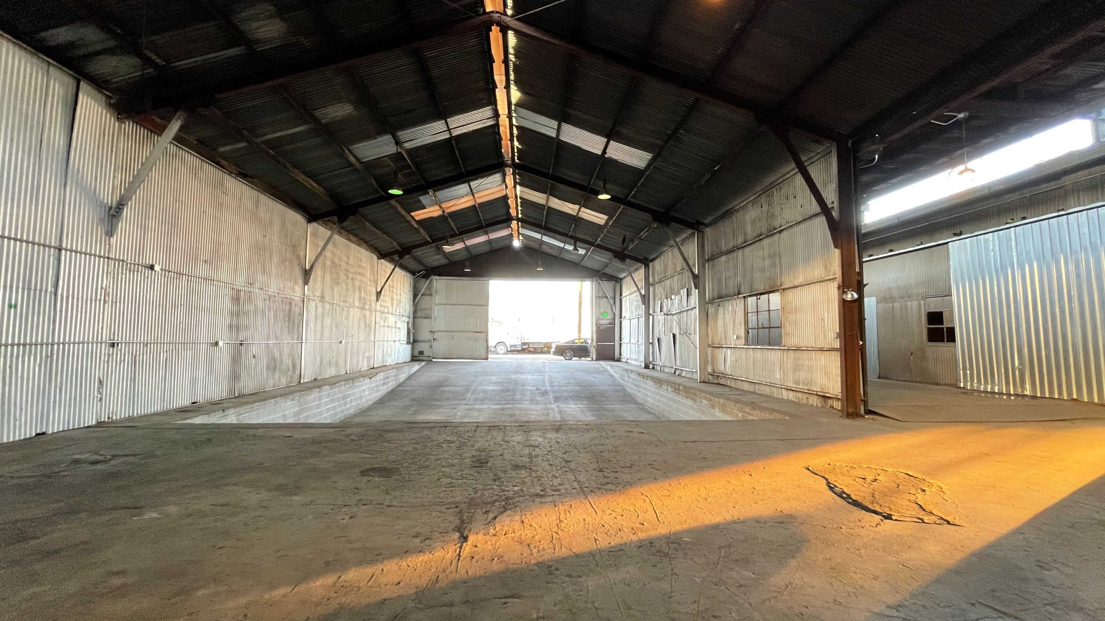 The interior of a large, empty warehouse with metal siding and a high, arched ceiling.