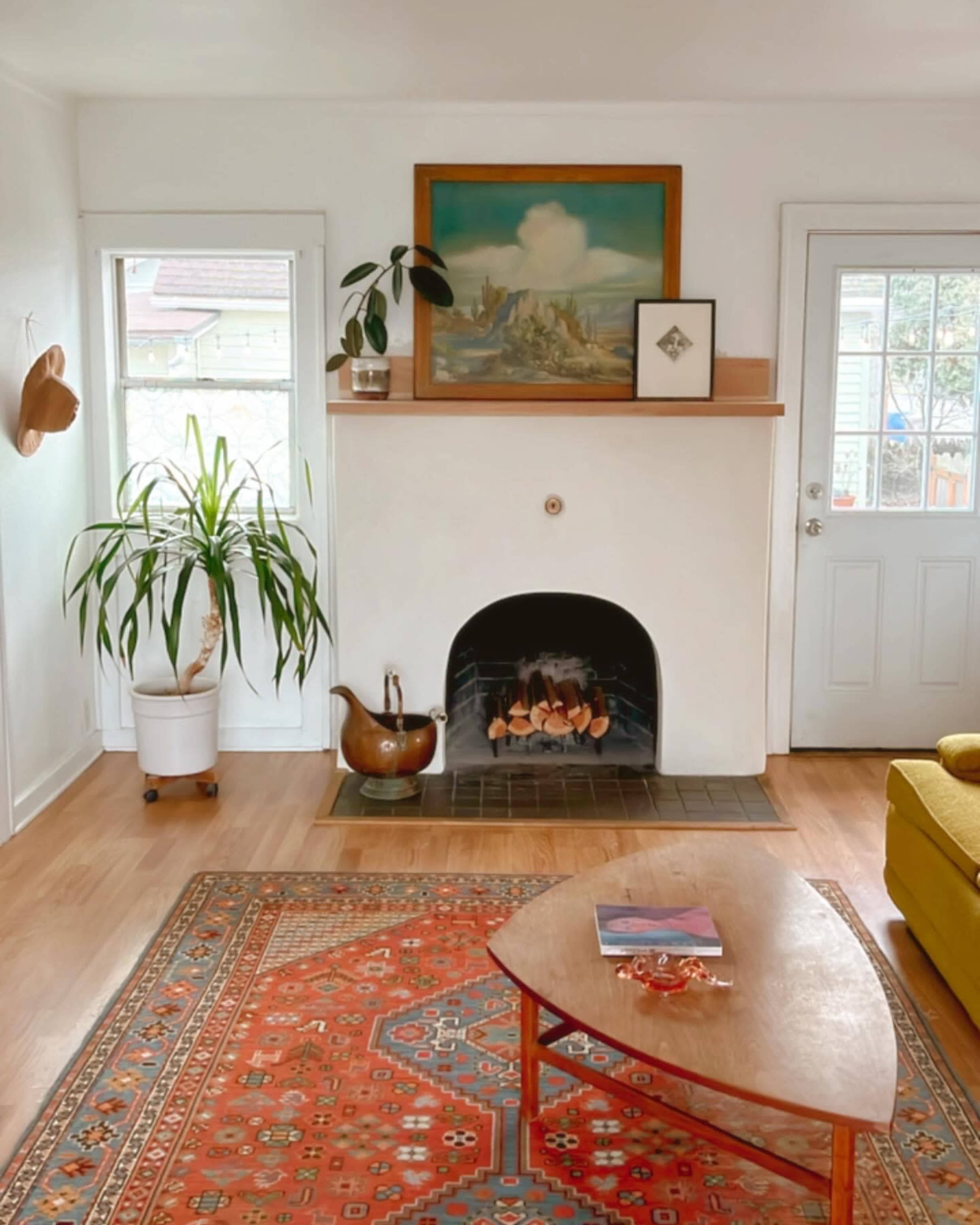 The scene features a cozy living room with a fireplace, a potted plant, a wooden coffee table, and a yellow sofa, accented by an area rug and artwork on the walls.